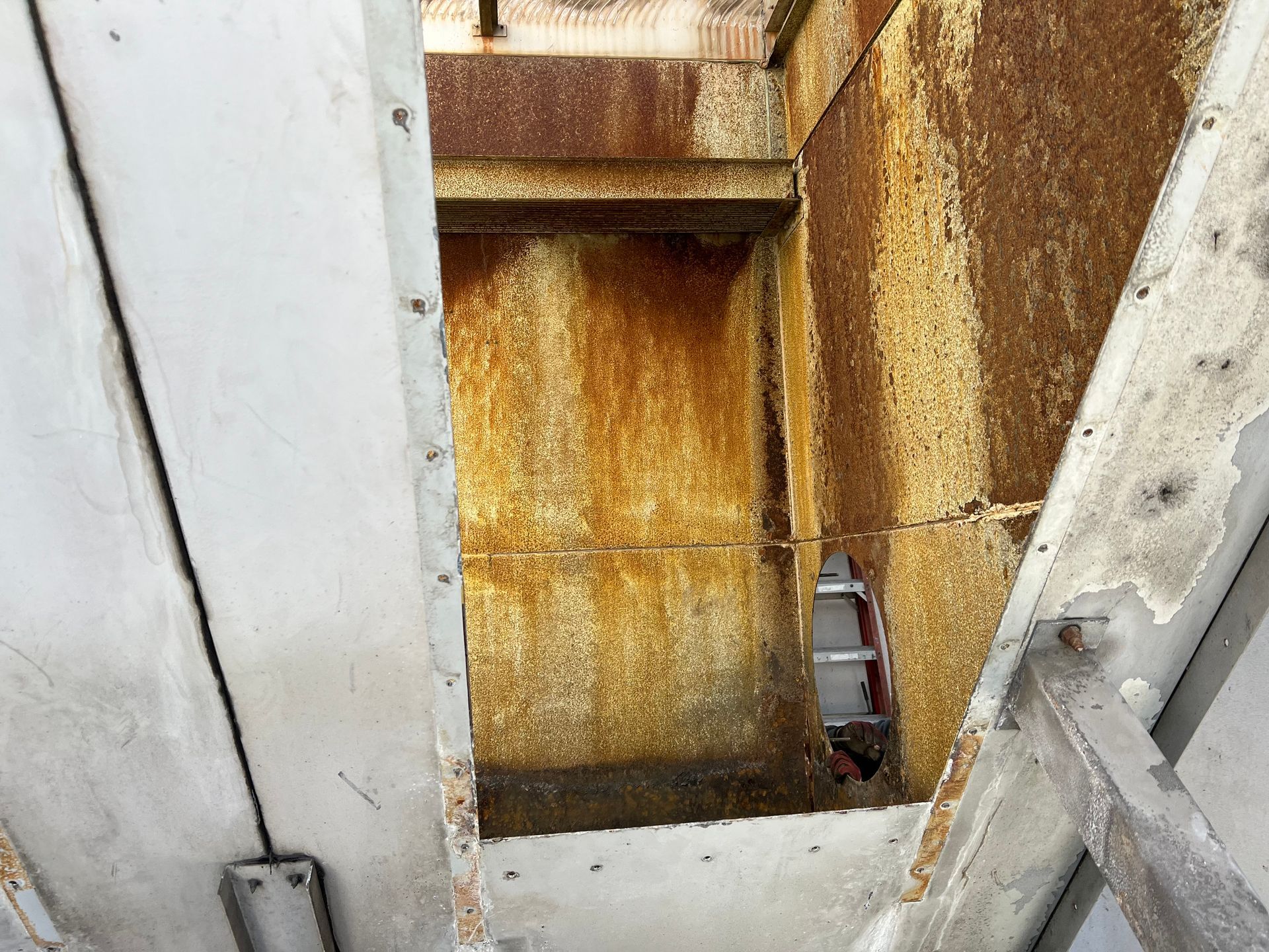 Rust-stained metal shaft between white panels, with a small pipe or fitting on the right.