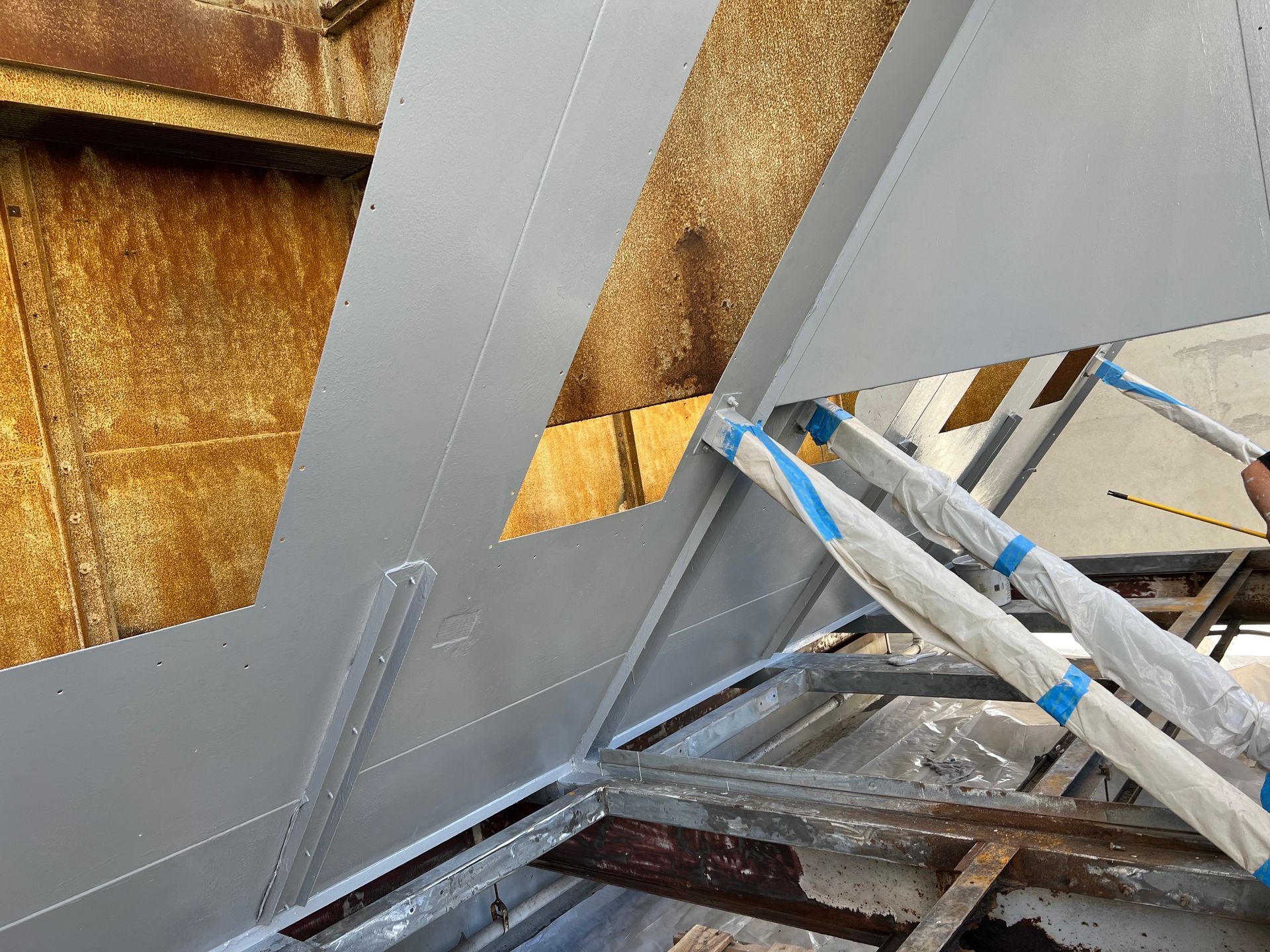 Metal roof panels under construction, with gray flashing and blue-taped scaffolding against a weathered wall