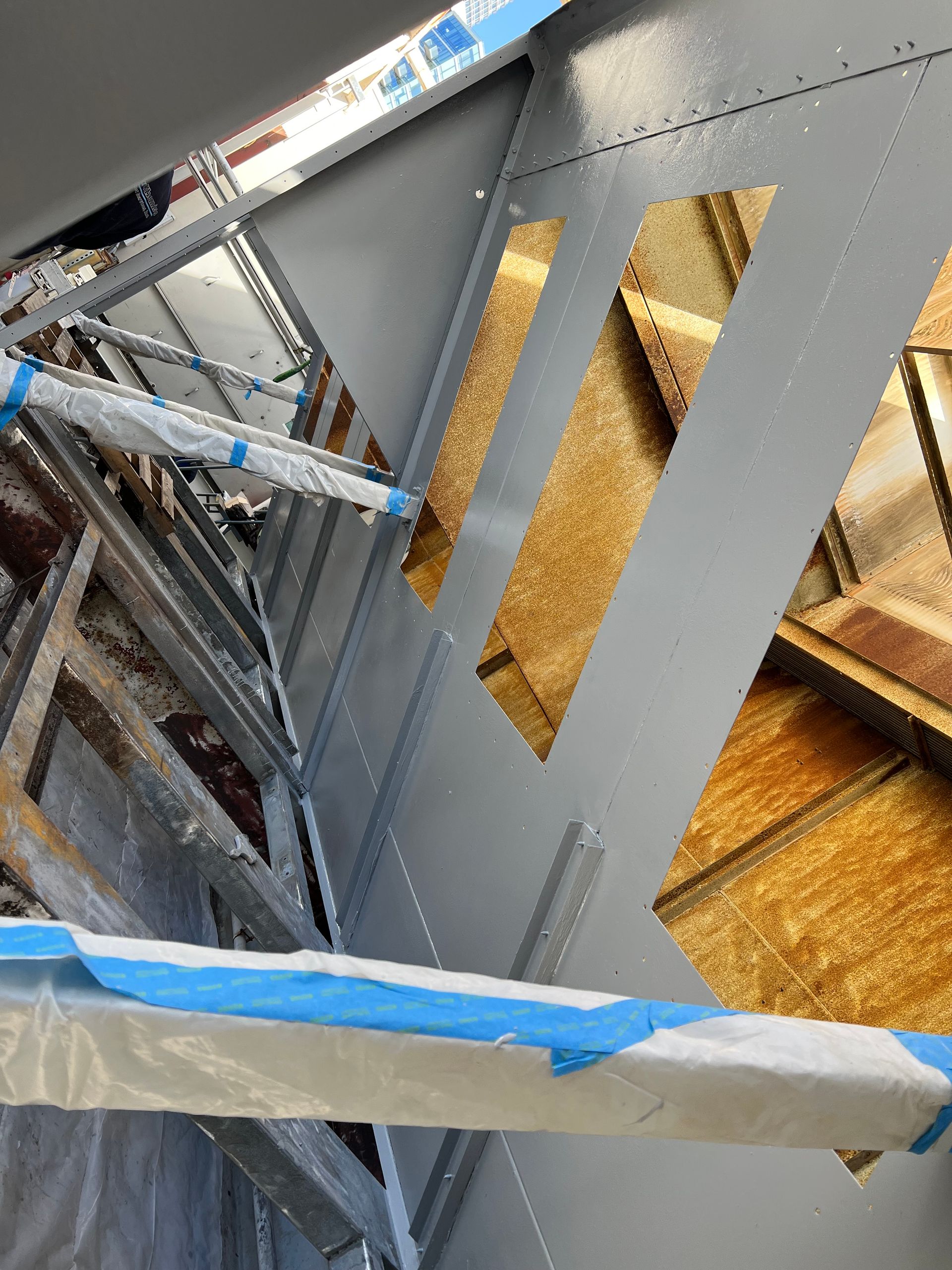 Blue-taped scaffolding beside a gray metal panel with rectangular cutouts in a construction area
