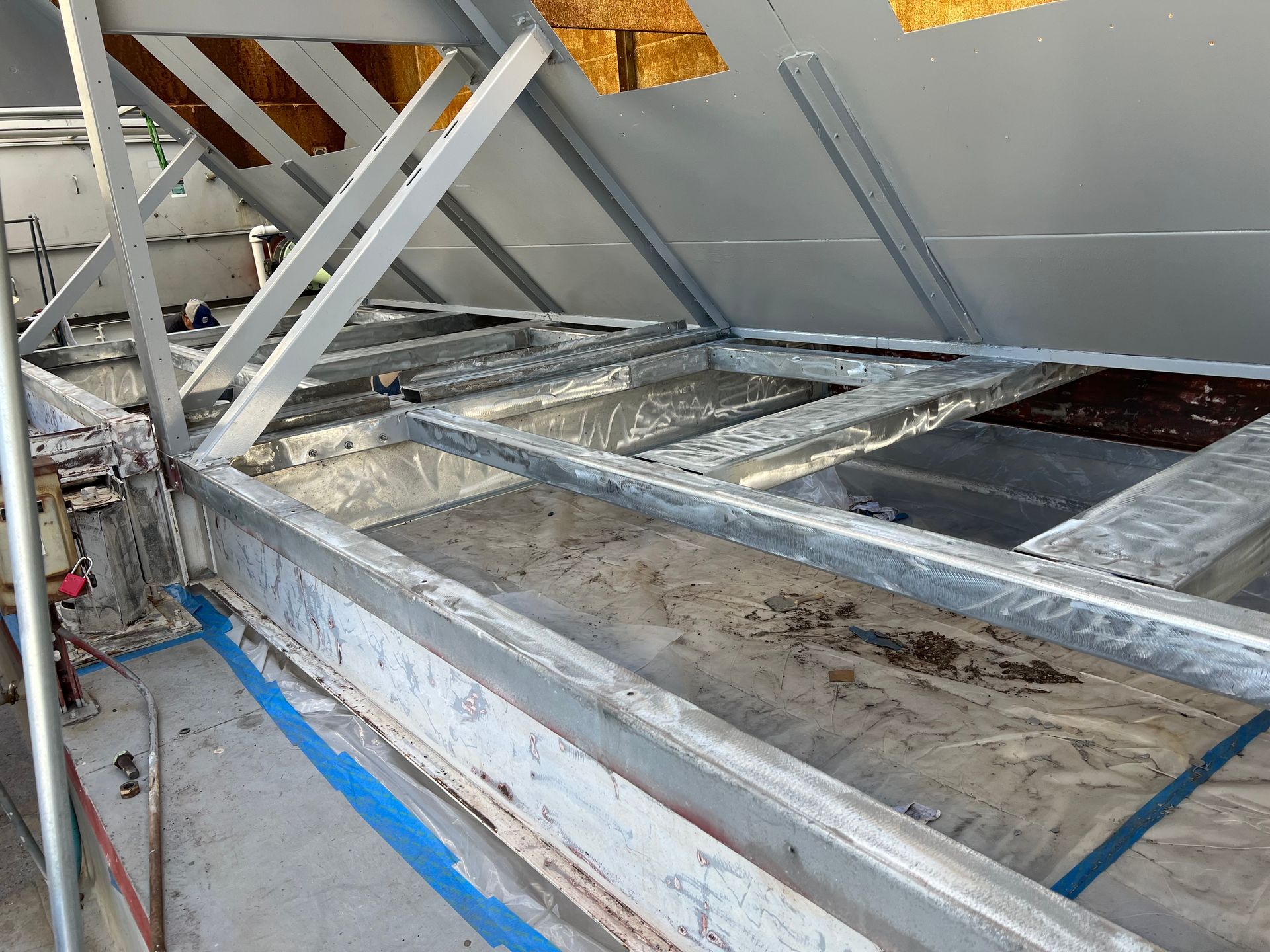 Damaged metal roof framing with torn white membrane and visible debris on a flat rooftop