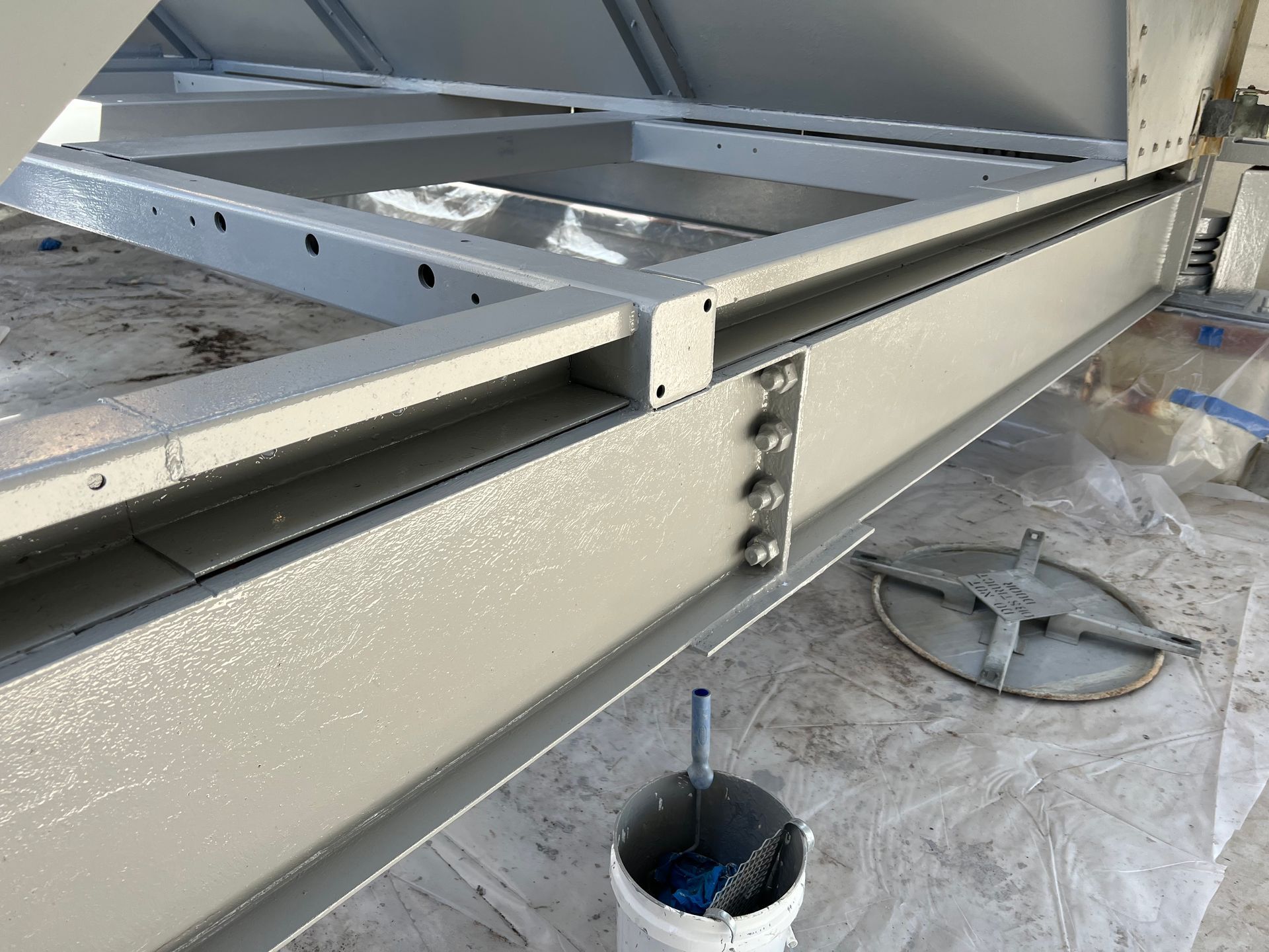 Metal beam construction detail with bolts, a protruding rod, and a ladder in a workshop setting