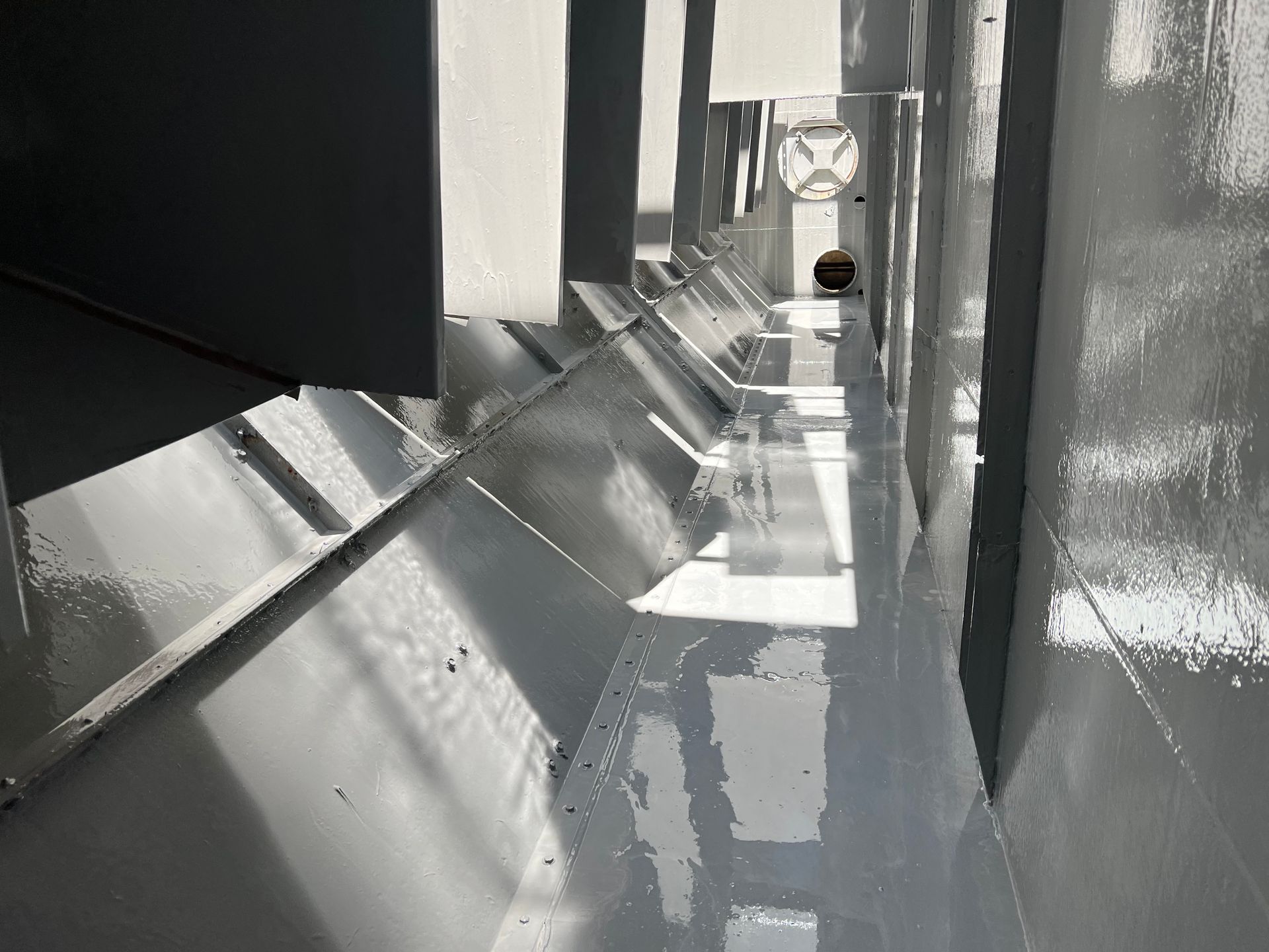 Narrow gray industrial corridor with reflective slanted panels and a small object at the far end
