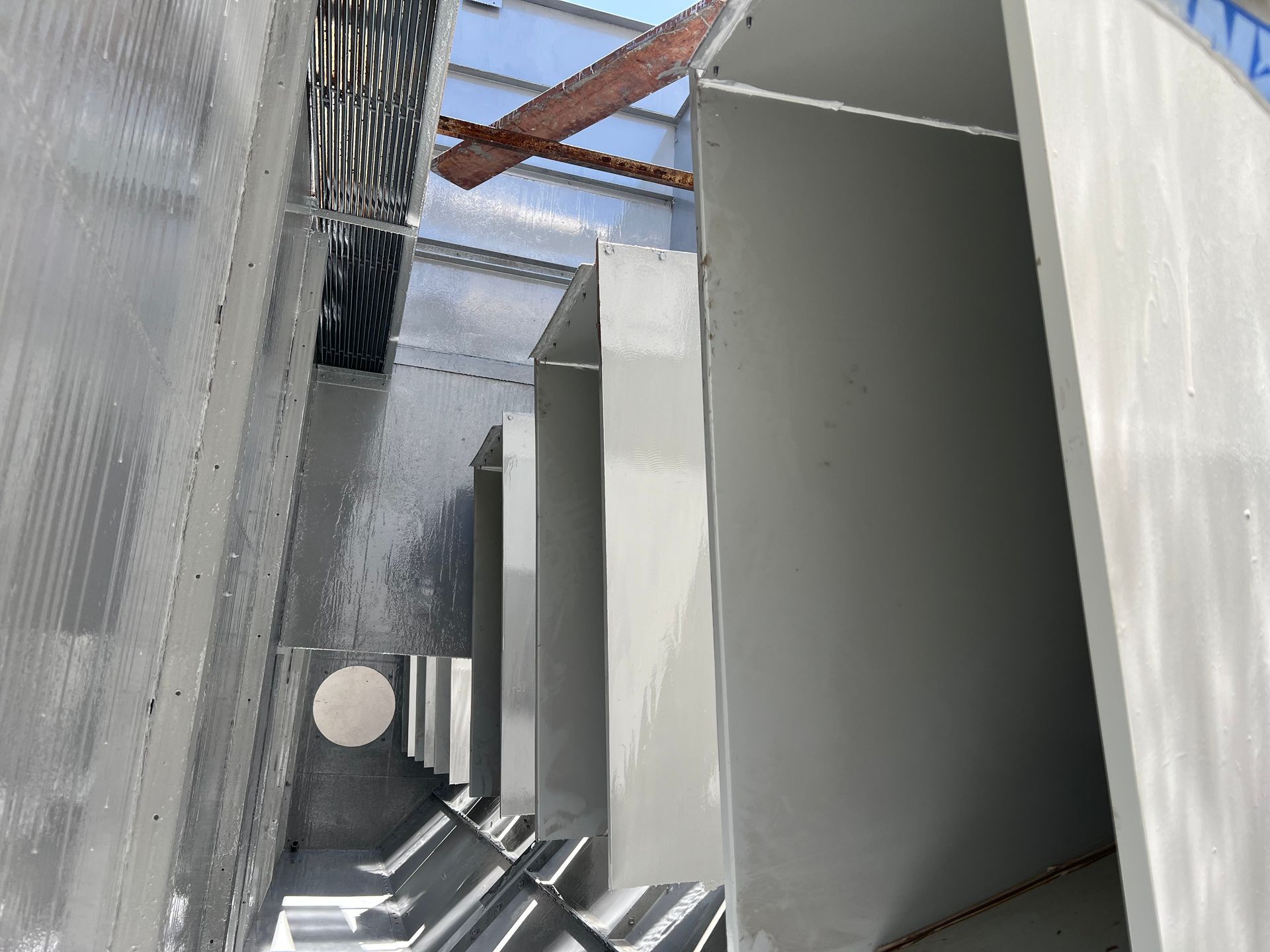 Narrow industrial corridor with tall metal panels and overhead beams in a dim, unfinished structure