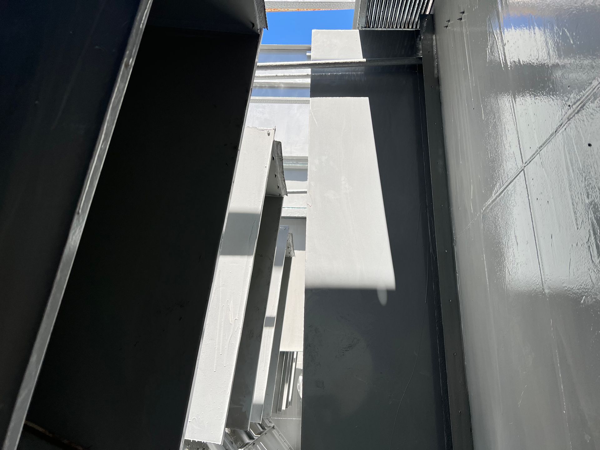 Narrow alley between tall gray buildings with blue sky visible overhead