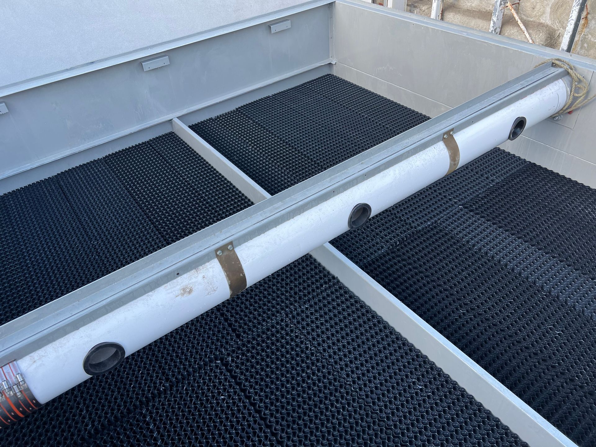 White PVC pipe with taped joints resting across a black mesh-lined tray or compartment
