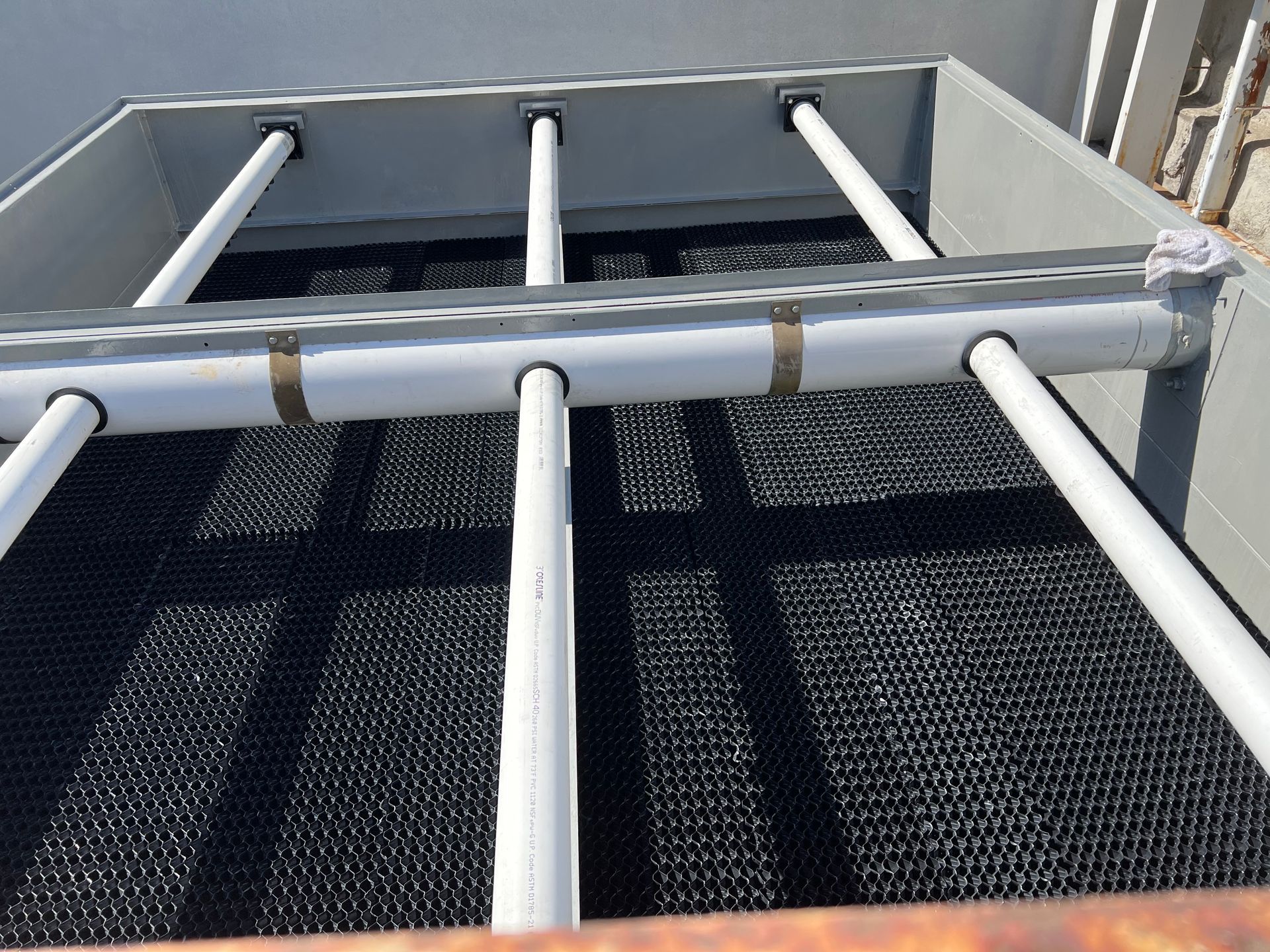 White PVC pipes forming a ladder-like structure over black mesh on a rooftop or industrial platform