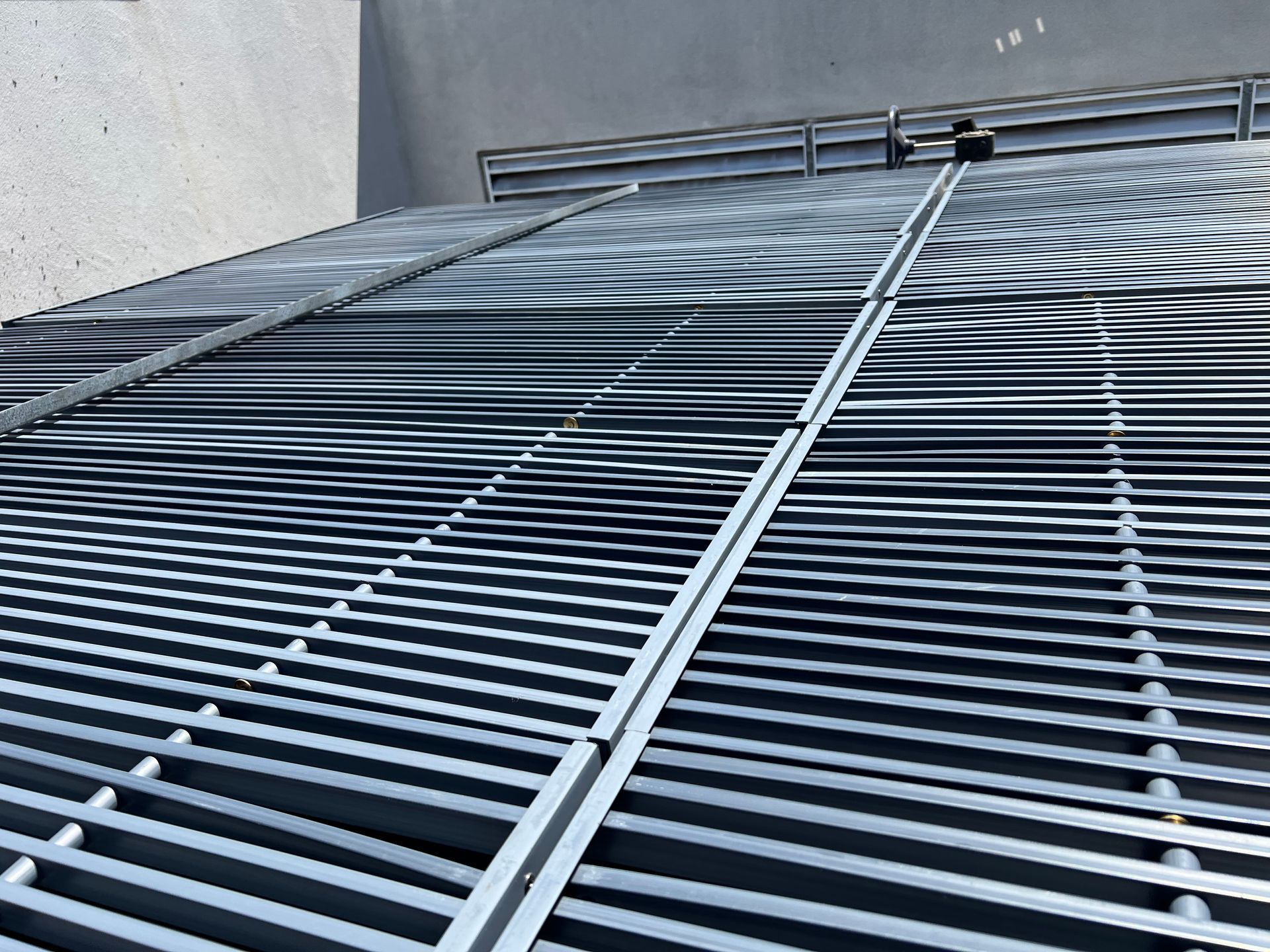 Metal roof grating with diagonal support rails beside a gray wall and vented structure