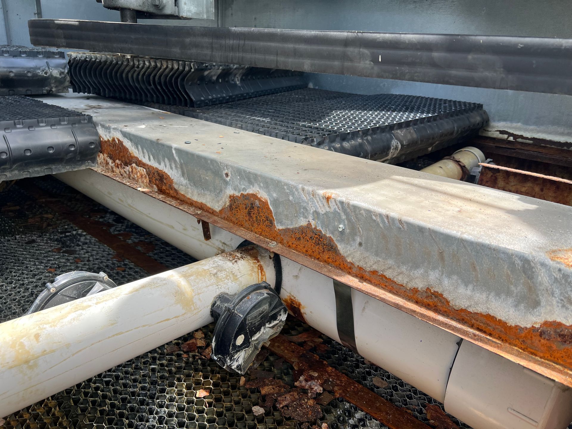 Rusty corroded metal beam with peeling white paint and pipes in an industrial setting