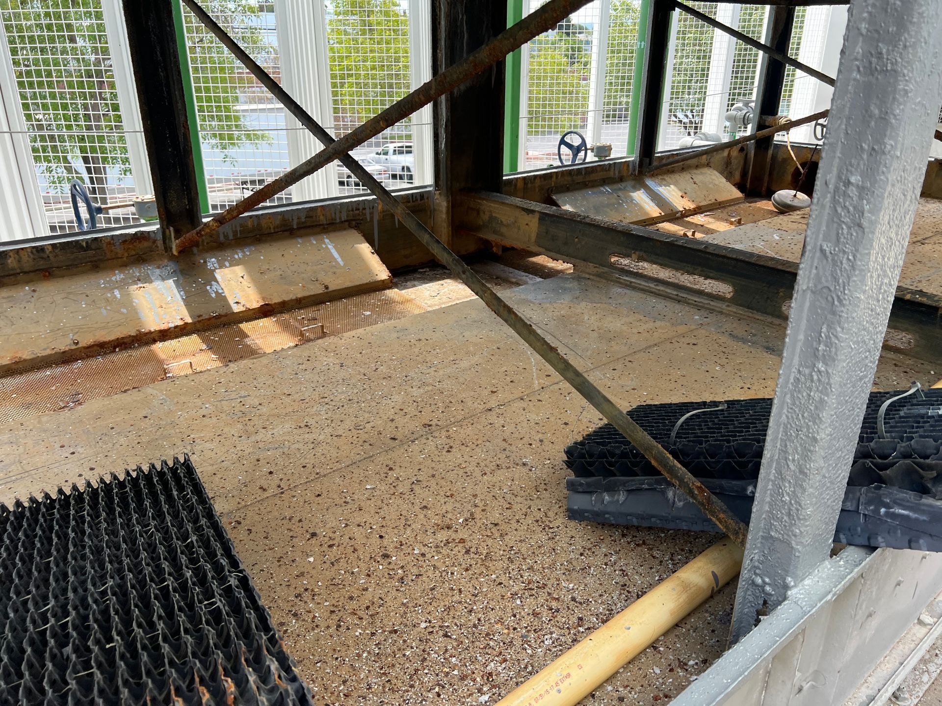Indoor industrial space with gravel floor, metal beams, and sunlight through windowed walls