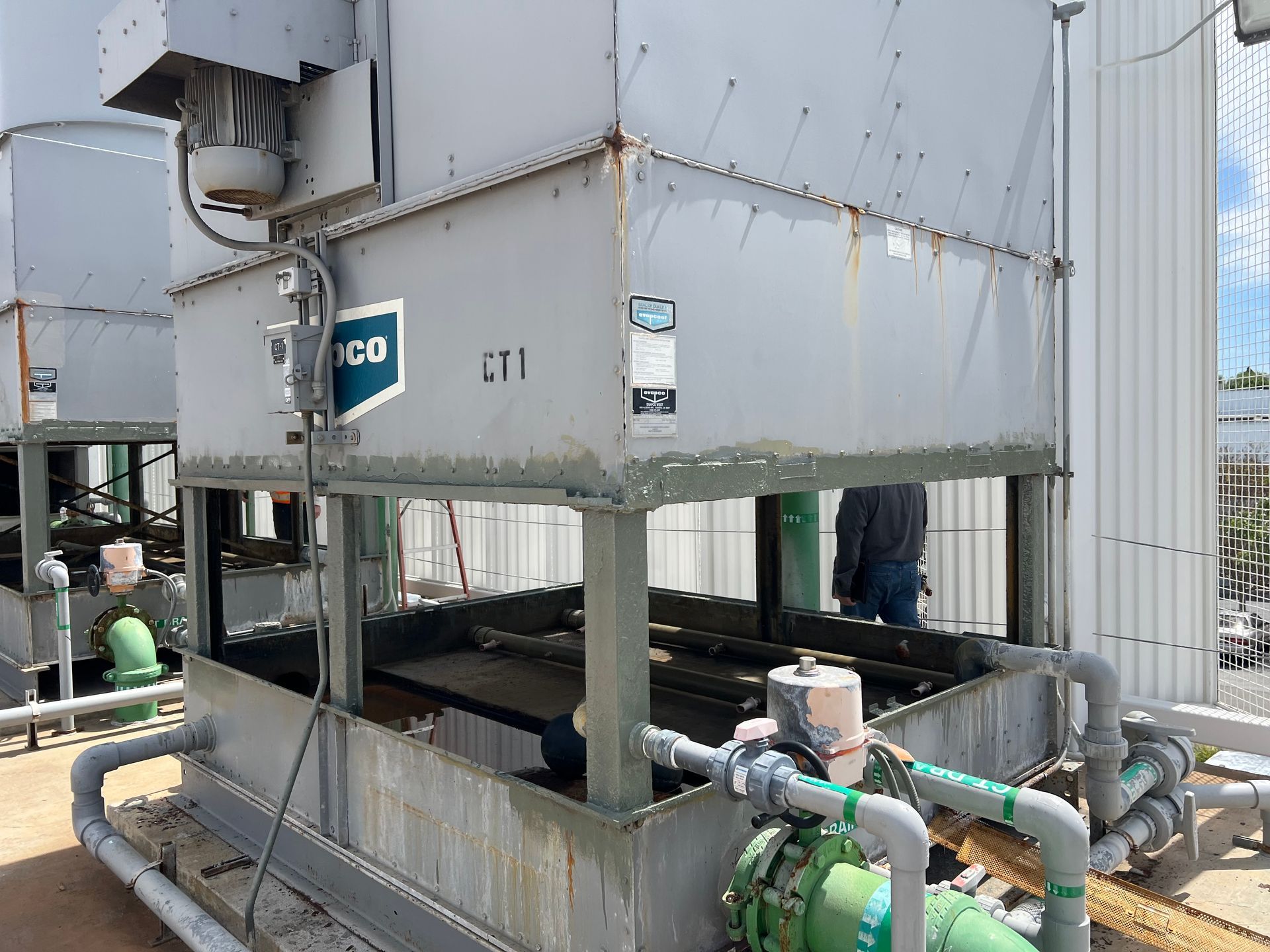 Large gray industrial cooling tower with pipes and machinery in an outdoor facility