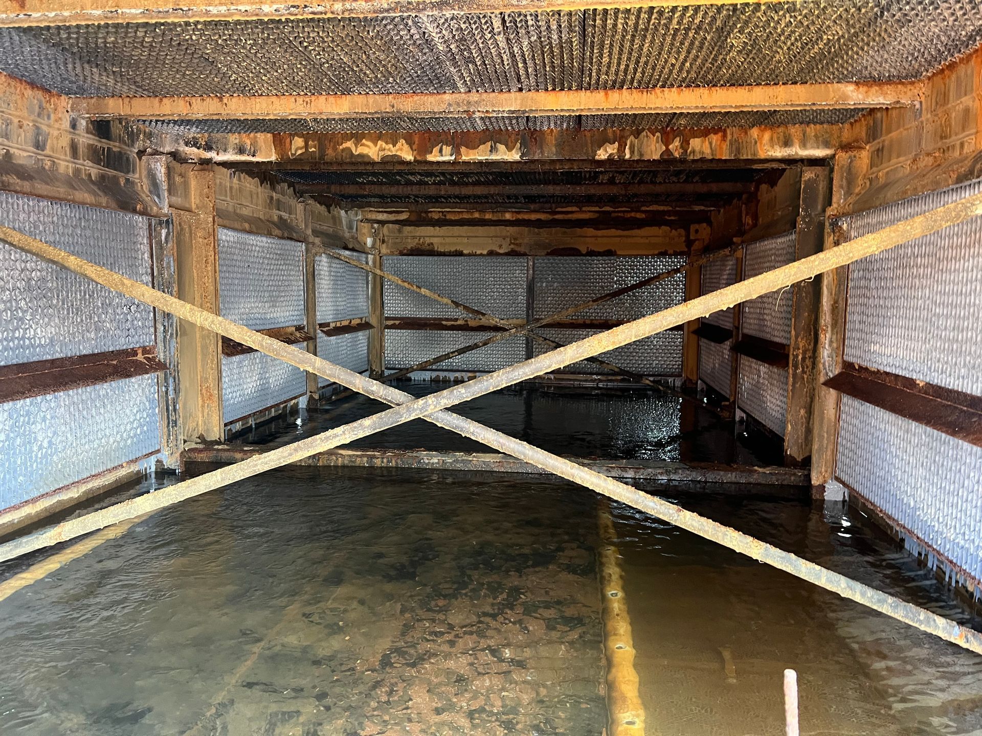 Flooded wooden tunnel with diagonal support beams and reflective water on the floor
