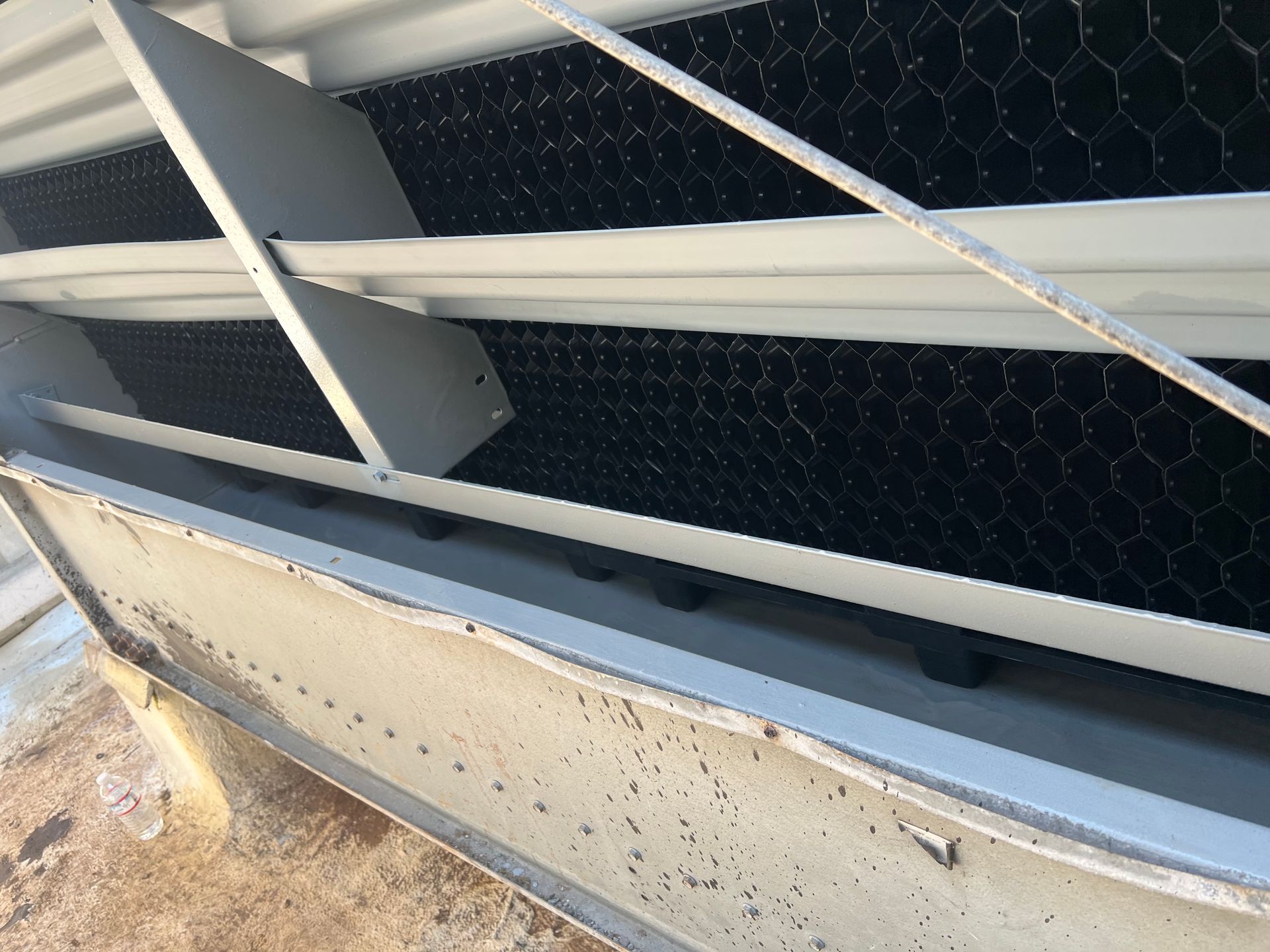 Close-up of a white metal structure with black hexagonal mesh and dust specks, outdoors.