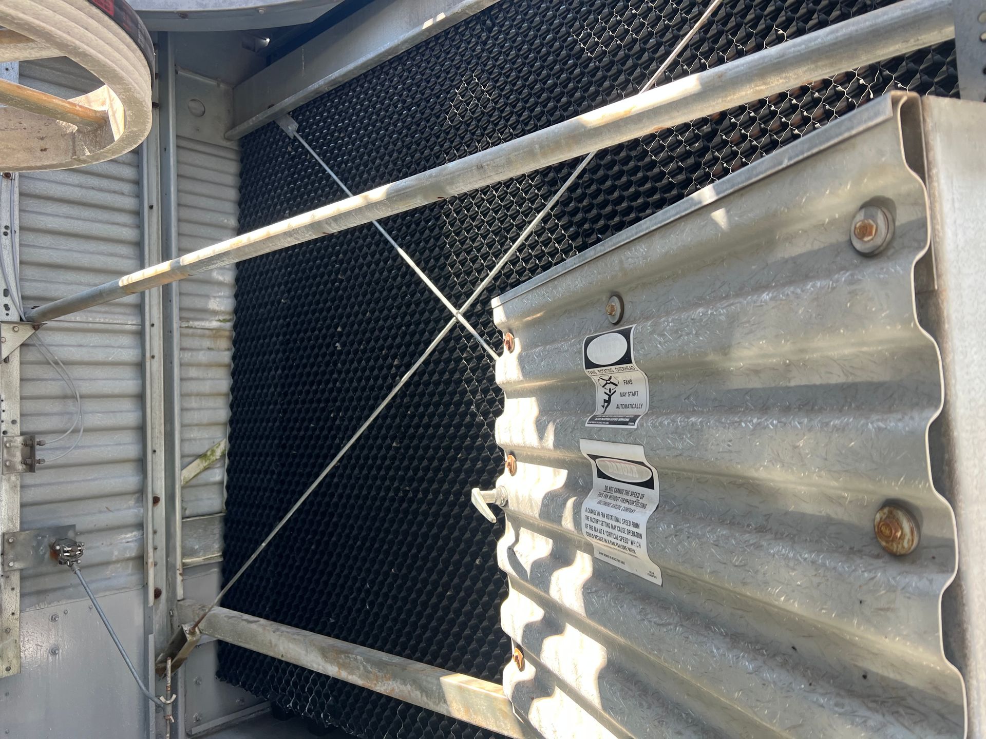 Metal corrugated barrier beside a chain-link fence and industrial equipment in a narrow outdoor area