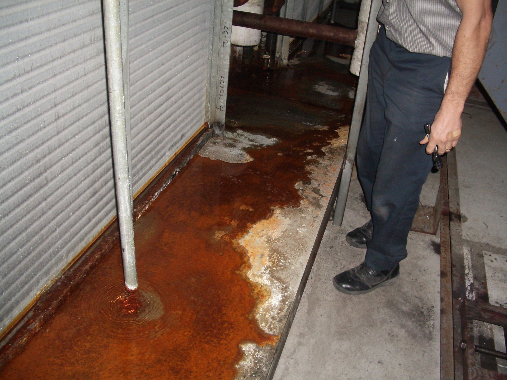 Rust-colored water leaking across a narrow sidewalk beside a storefront; a person stands nearby.