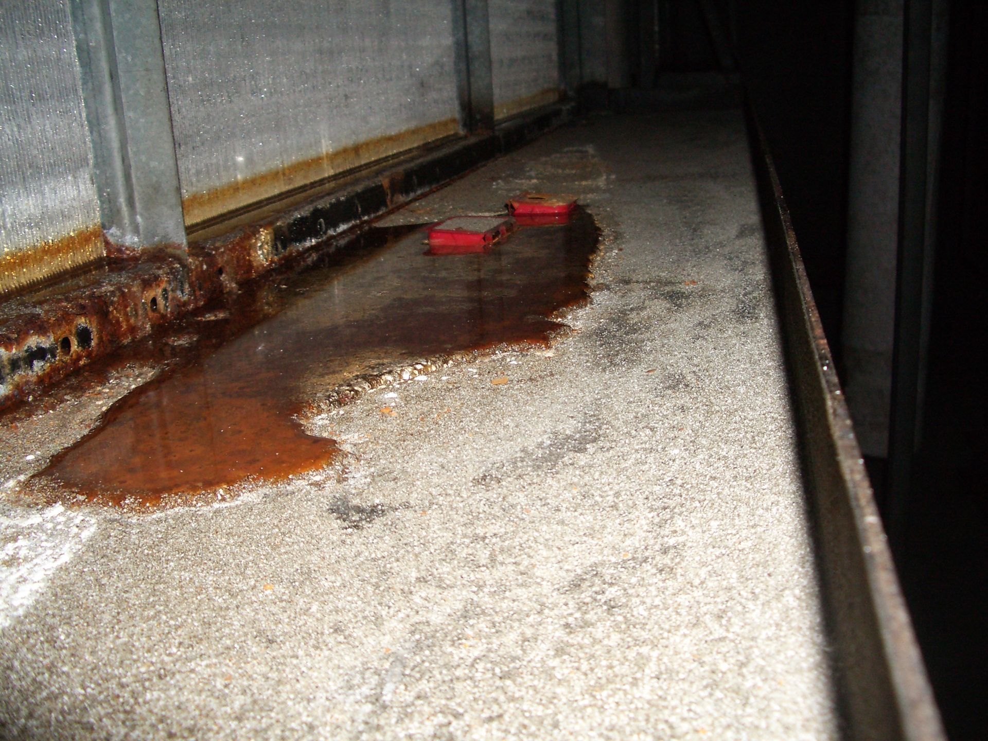 Brown spill on a concrete floor beside a wall, with a small red object in the background
