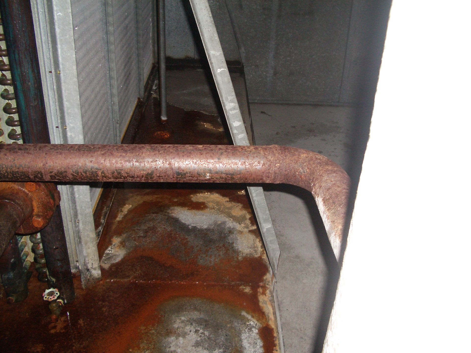 Rusty metal bar and pipes in a narrow industrial space with corrugated walls and peeling rust on the floor.