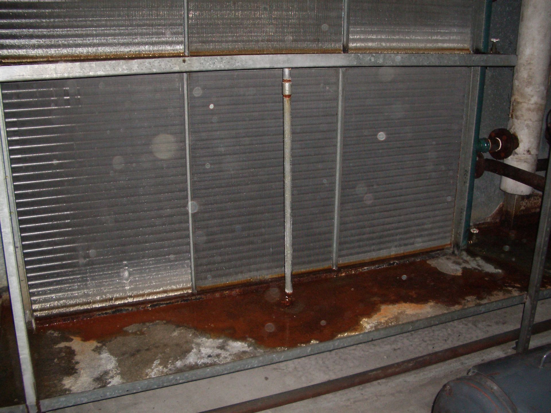Damaged industrial radiator with rust stains and water pooling on the floor
