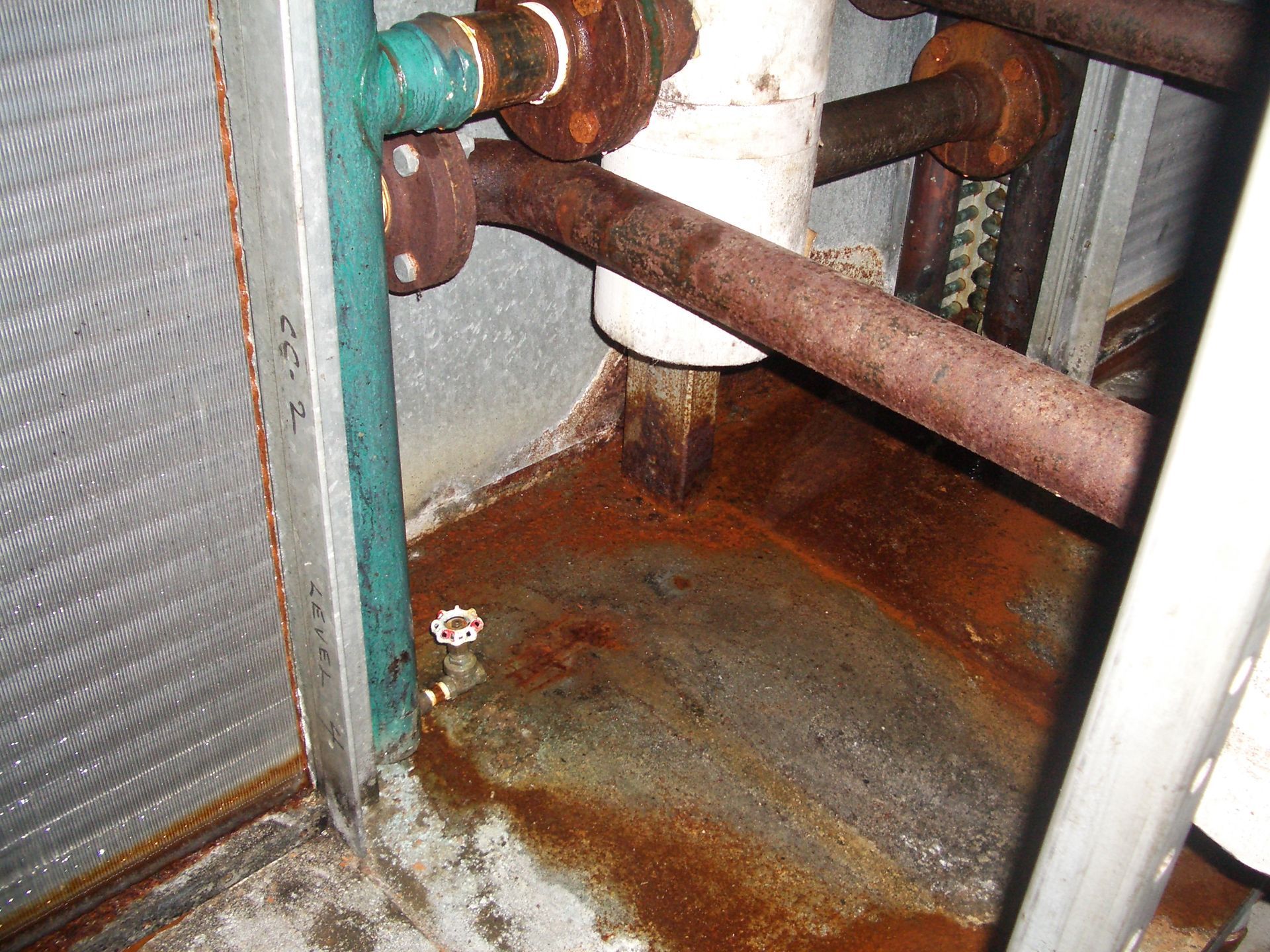 Rusty pipes and corroded HVAC equipment with water damage and discoloration around the base.
