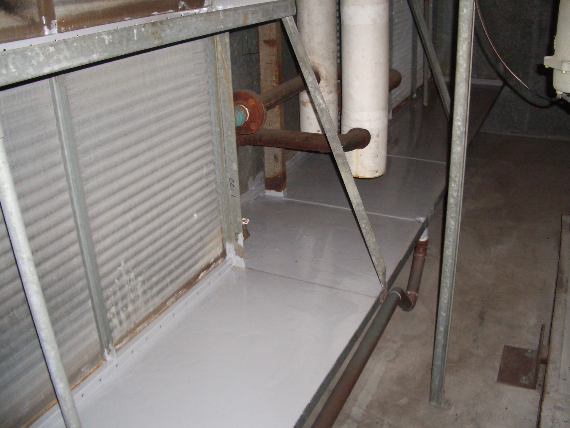 Industrial equipment and metal framework in a utility room, with a white panel and pipes visible.