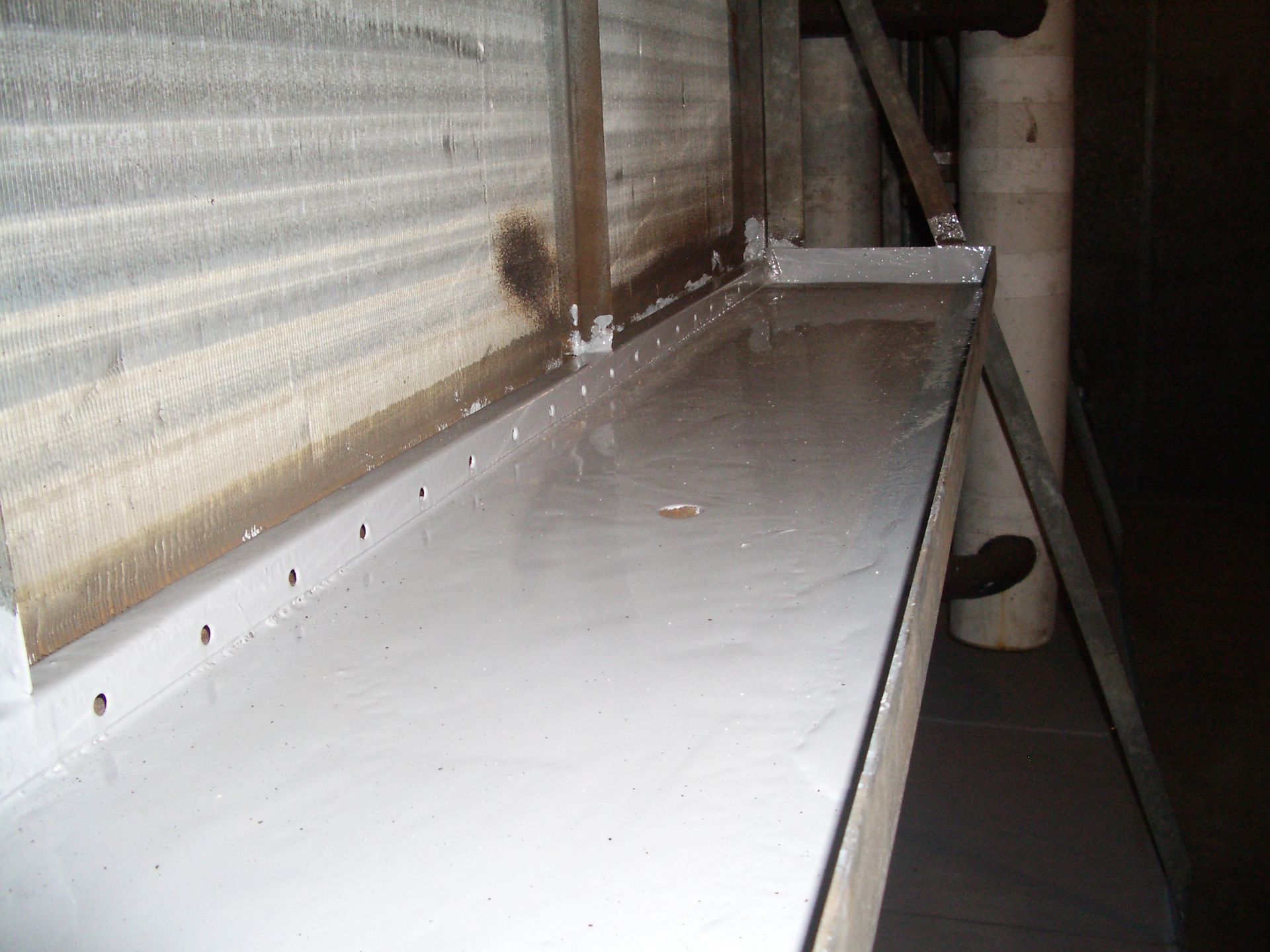 Empty metal shelf in a narrow industrial space with white walls and a dark floor opening.