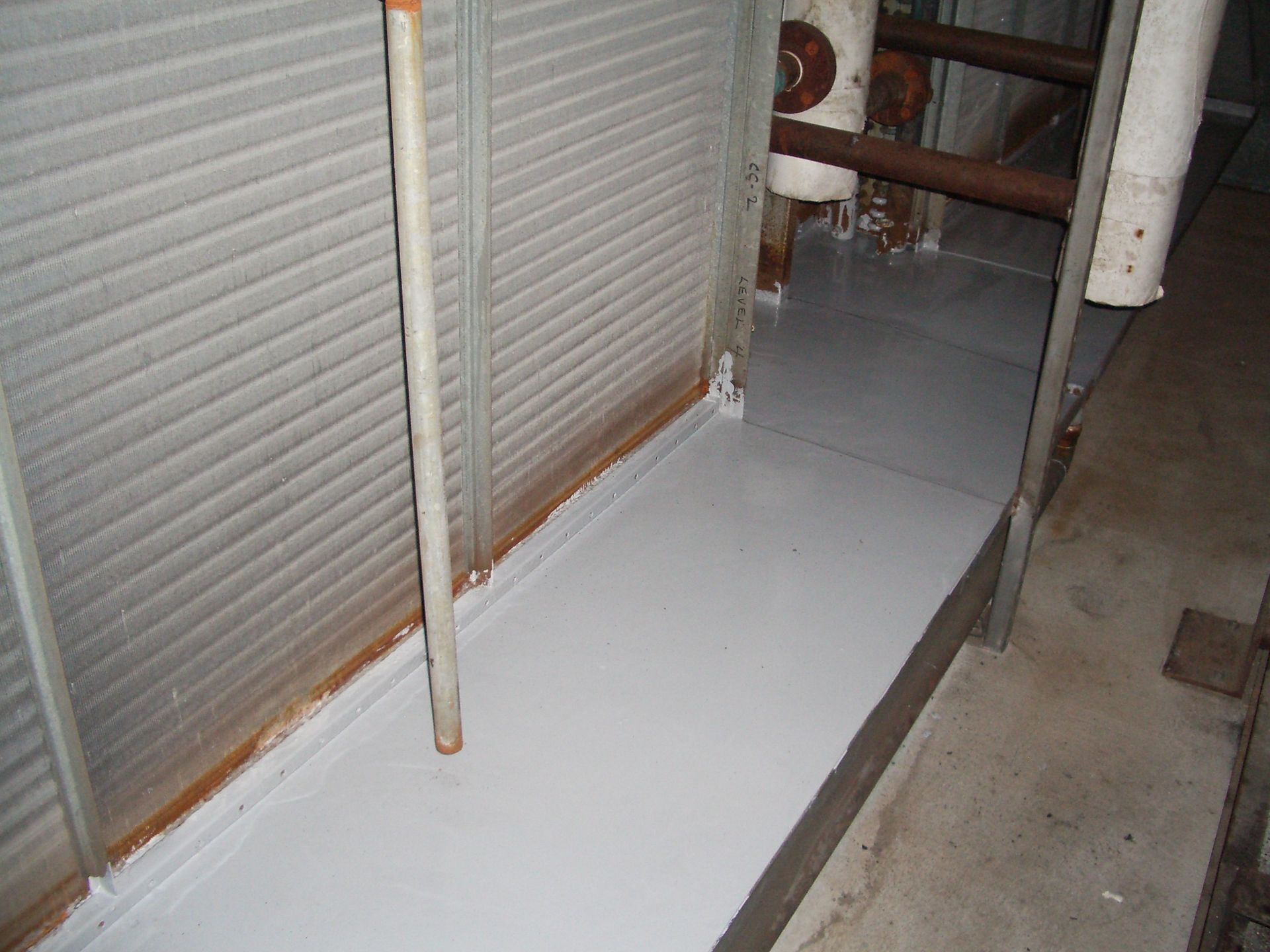 Freshly painted white floor beside closed metal shutters and exposed pipes in a narrow utility area