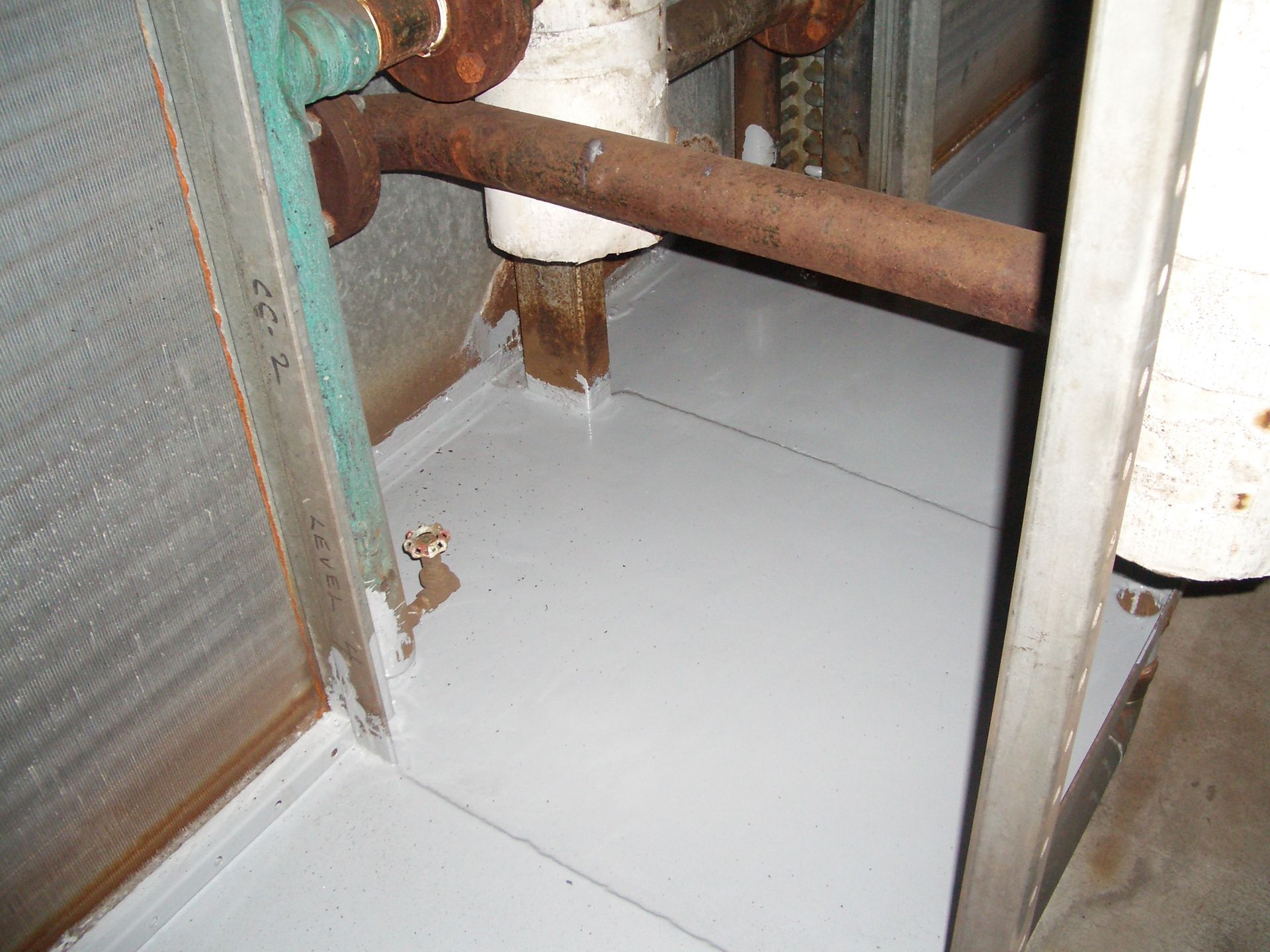 Rusty pipes and a white floor inside a narrow industrial utility space.