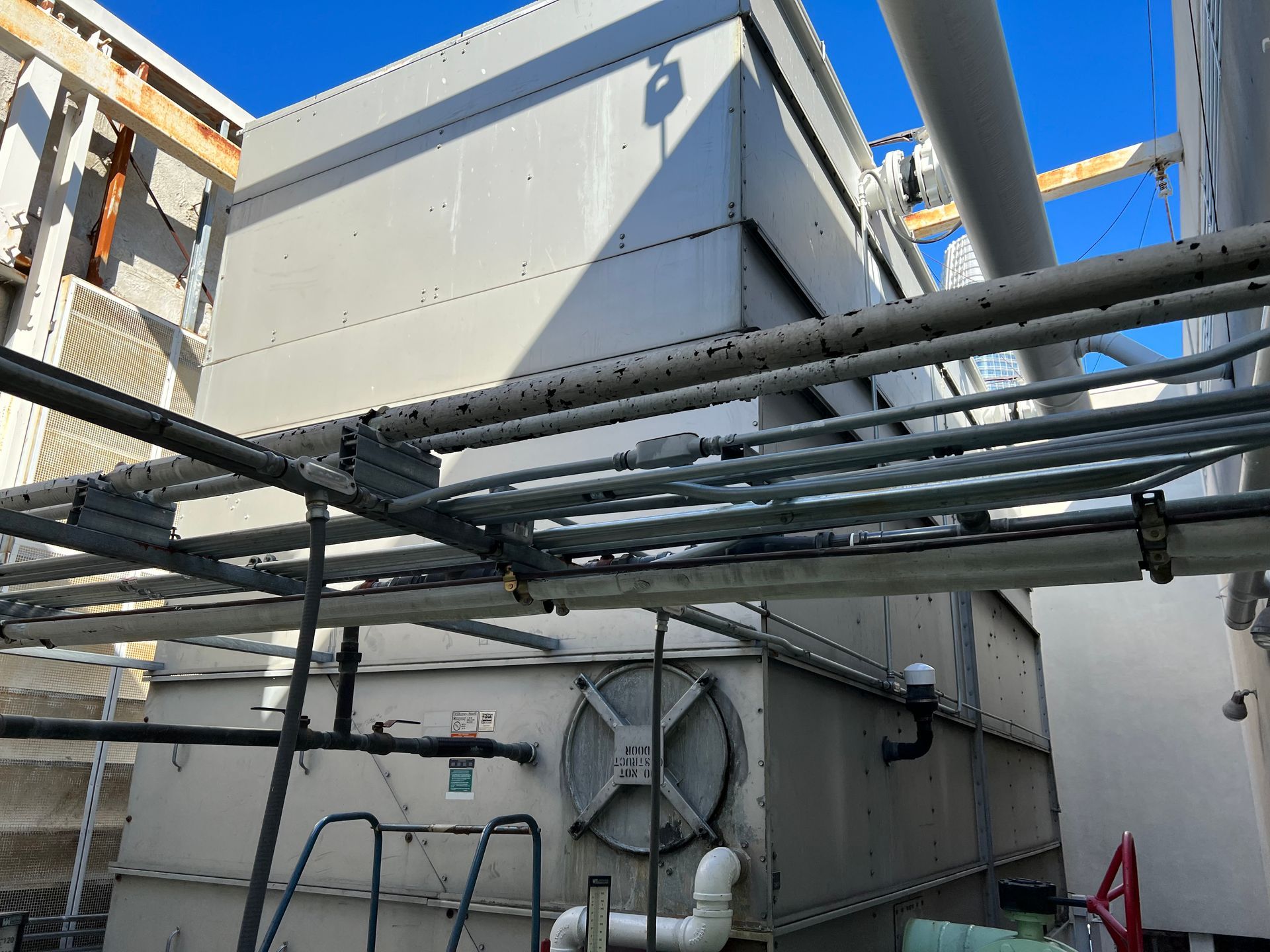 Industrial rooftop equipment with gray HVAC units and overhead pipes under a blue sky
