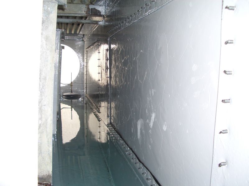 Interior of a metal tank with shiny, painted walls. Circular openings are visible along one side.