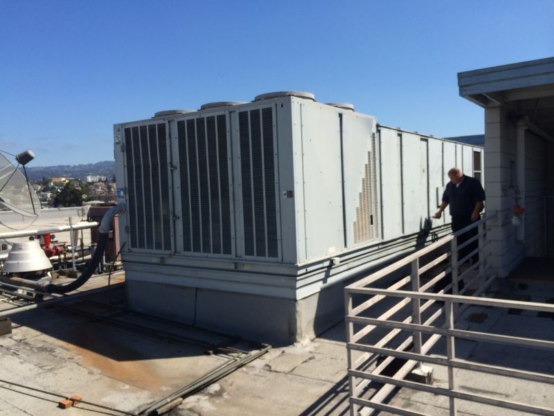 HVAC unit on a rooftop with a person walking towards it, sunny day.