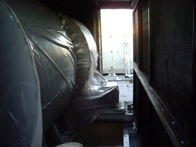 Inside industrial equipment: large, covered cylinders and open doorway with metal grating.