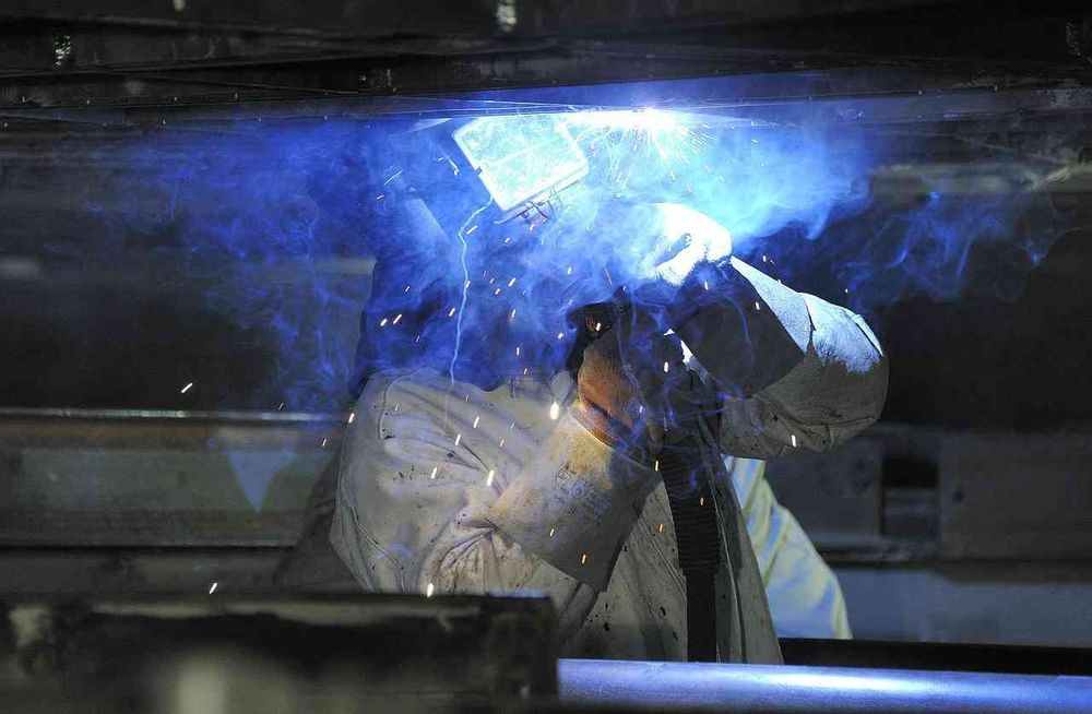 A man is welding a piece of metal in a factory.