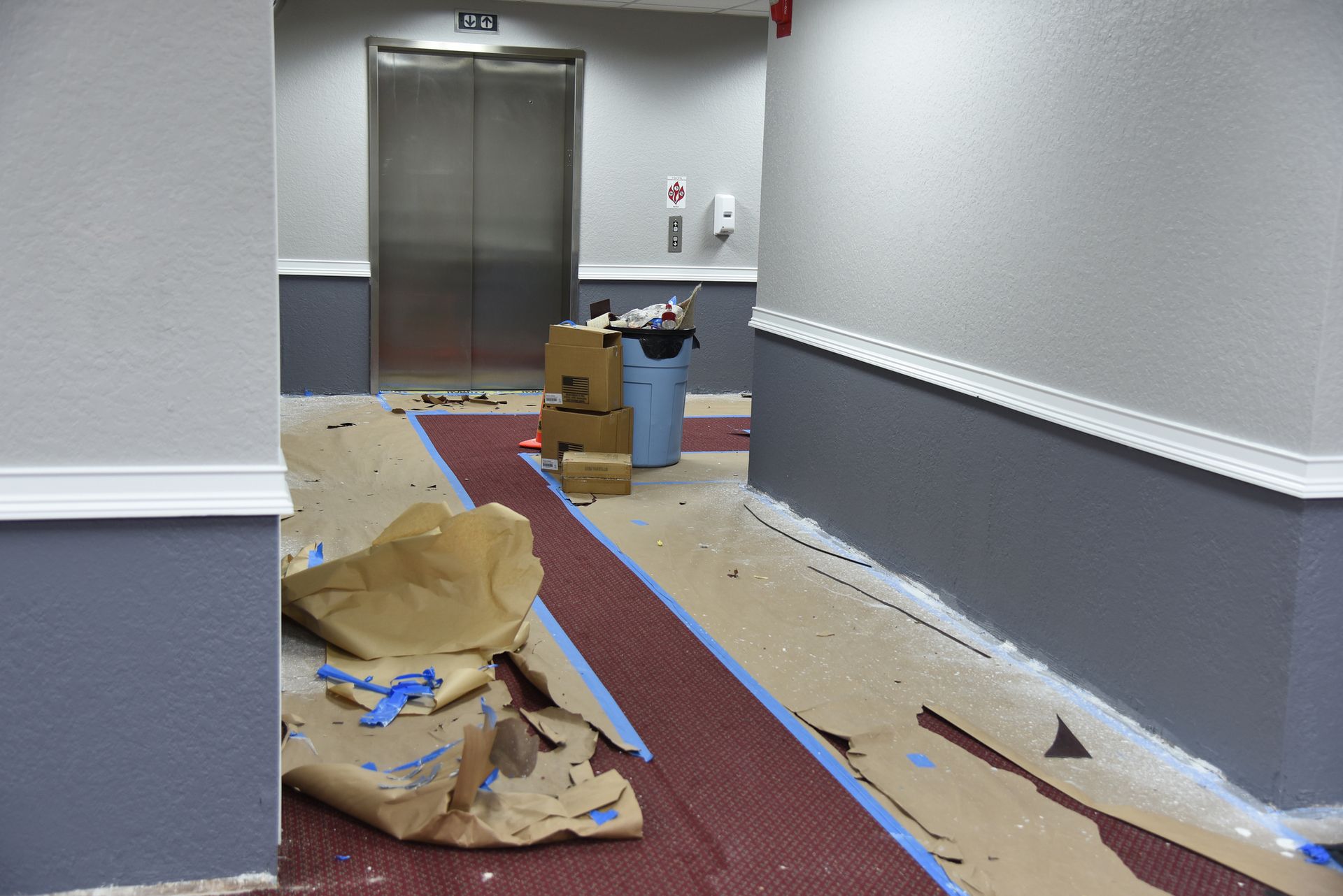 Renovation scene in a hallway with red carpet, covered in paper and tape.