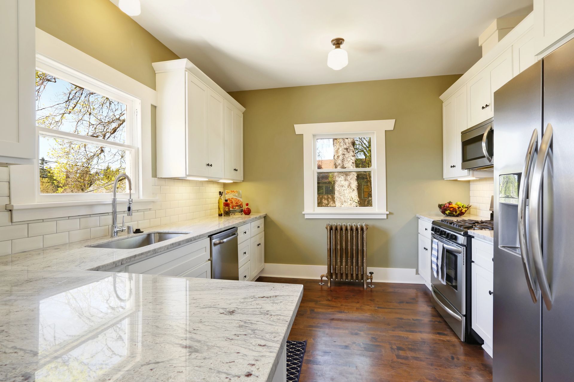 Bright modern kitchen with white cabinets, marble island, stainless steel appliances, and wood floors