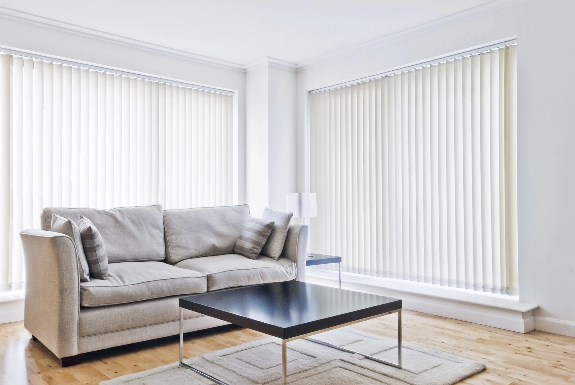 Bright living room with beige sofa, black coffee table, and large windows with vertical blinds