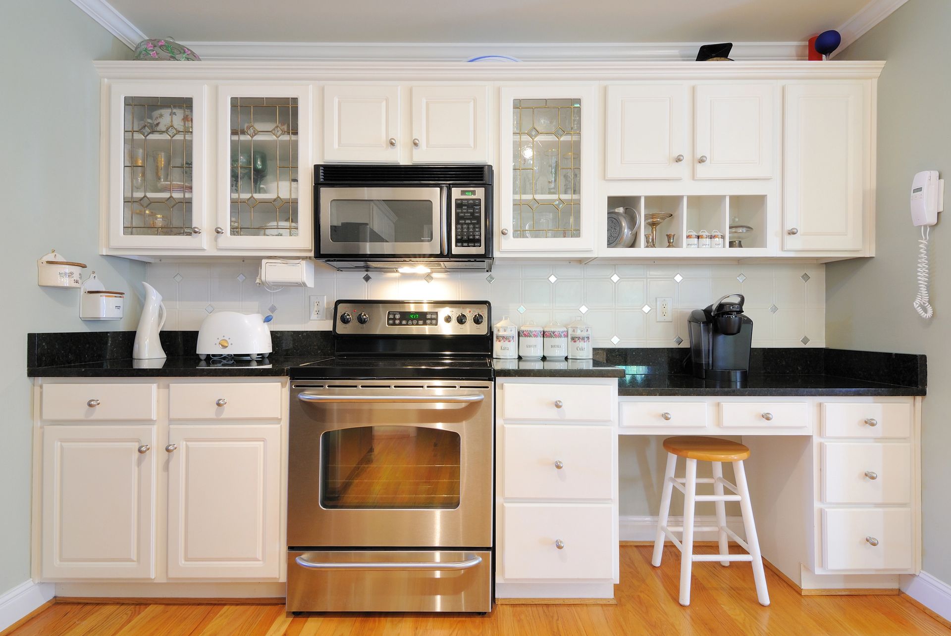 Bright kitchen with white cabinets, glass doors, stainless steel stove, and microwave.