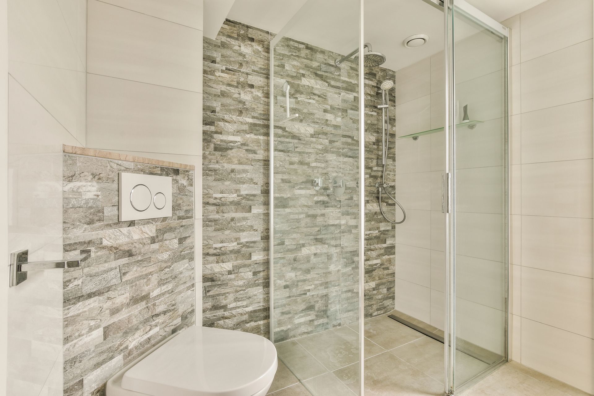 Modern bathroom with glass shower, stone tile accent wall, and wall-mounted toilet