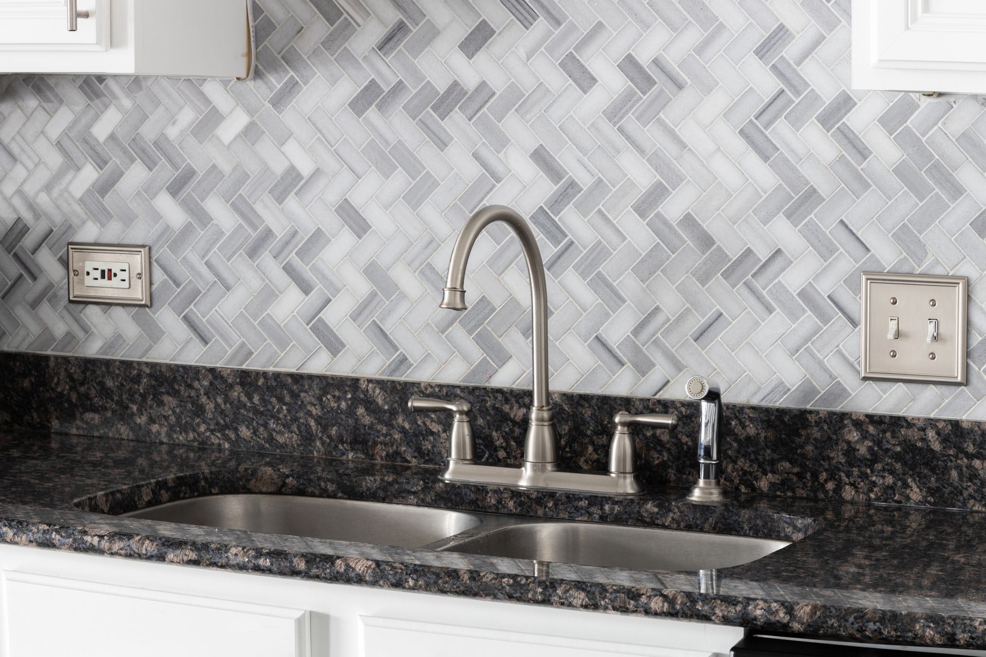 Modern kitchen sink with granite countertop, herringbone tile backsplash, and chrome faucet