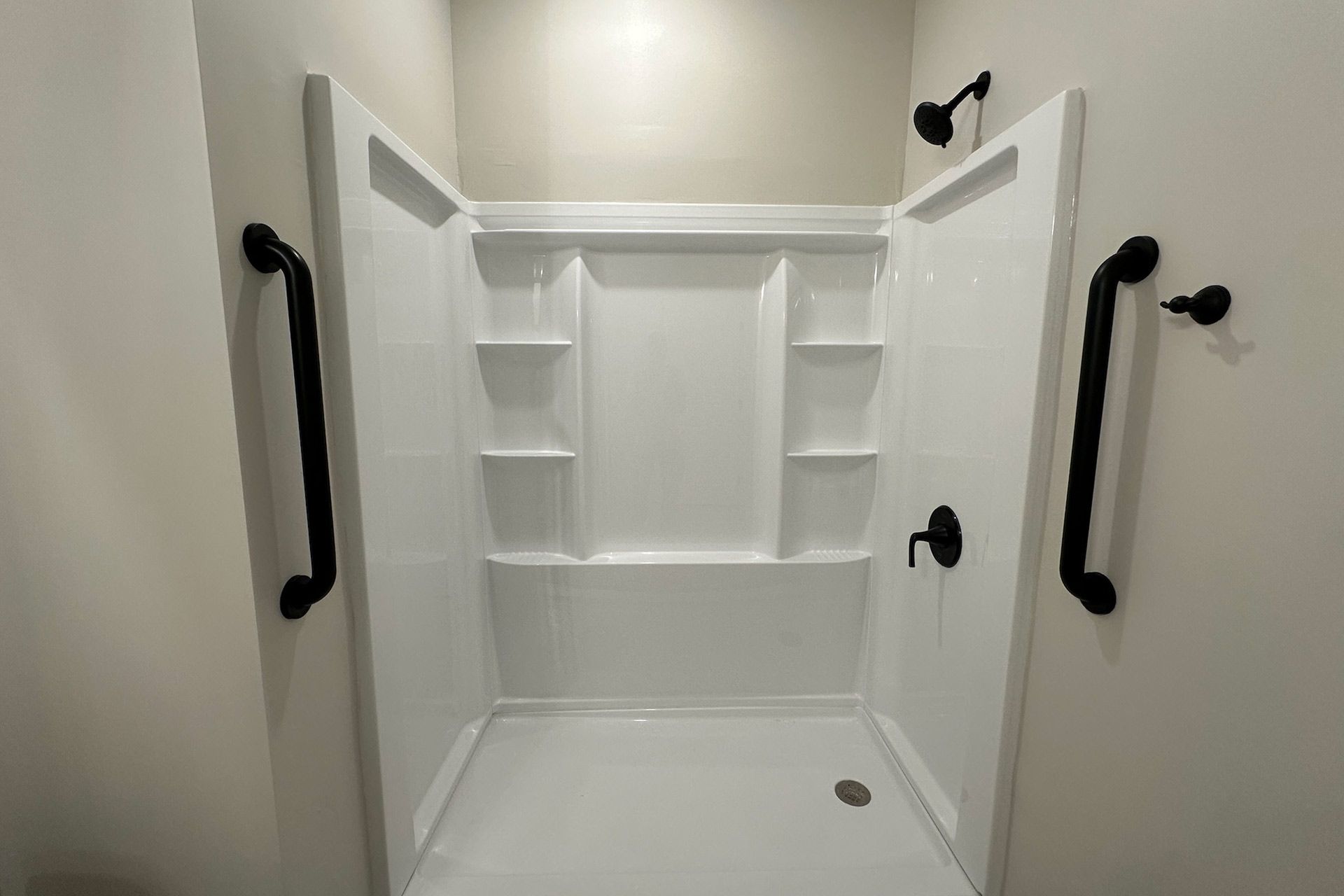 White accessible shower with black grab bars and fixtures.