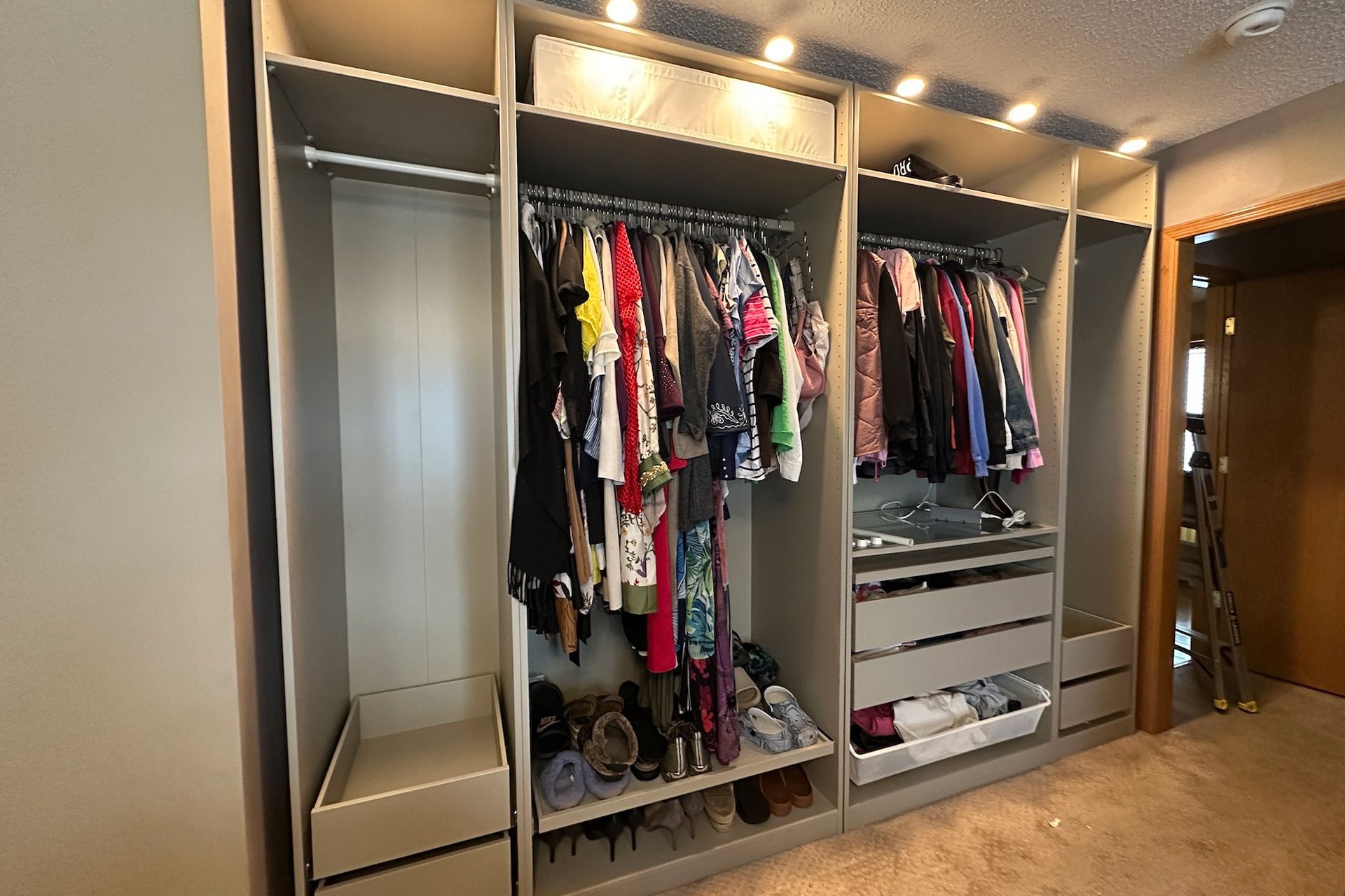 Built-in closet with clothes hanging, drawers, and shelving. Neutral color with overhead lighting.