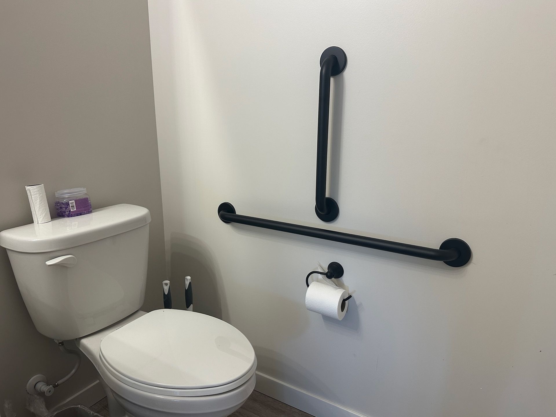 Bathroom with white toilet, black grab bars, and a toilet paper holder.