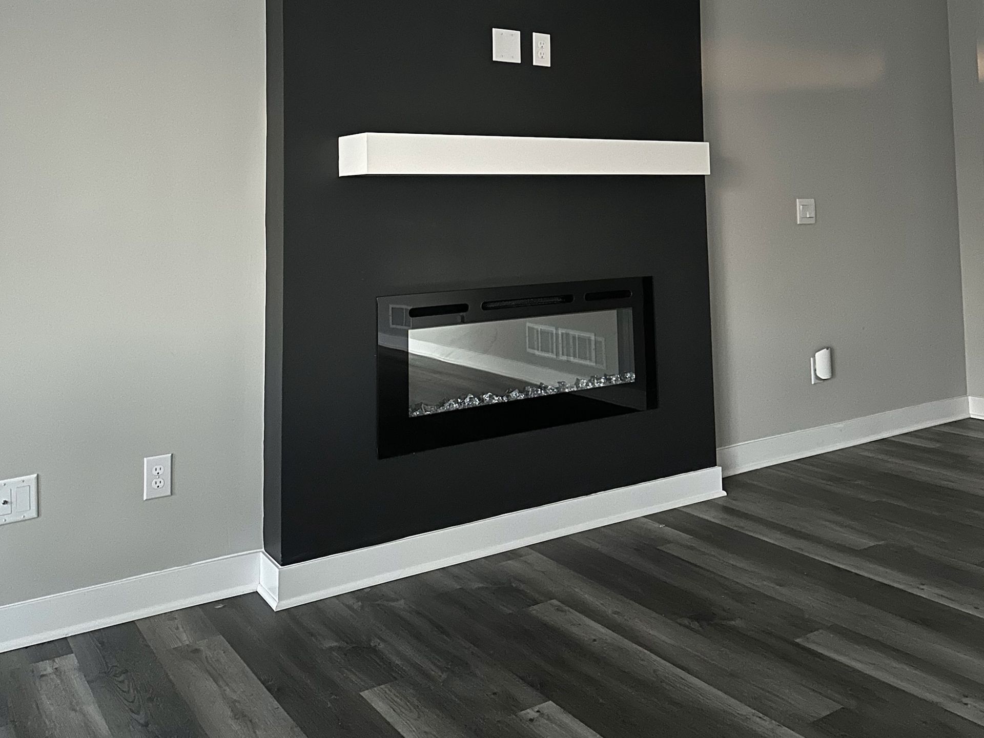Black fireplace with white mantel on gray wall; dark wood floor.