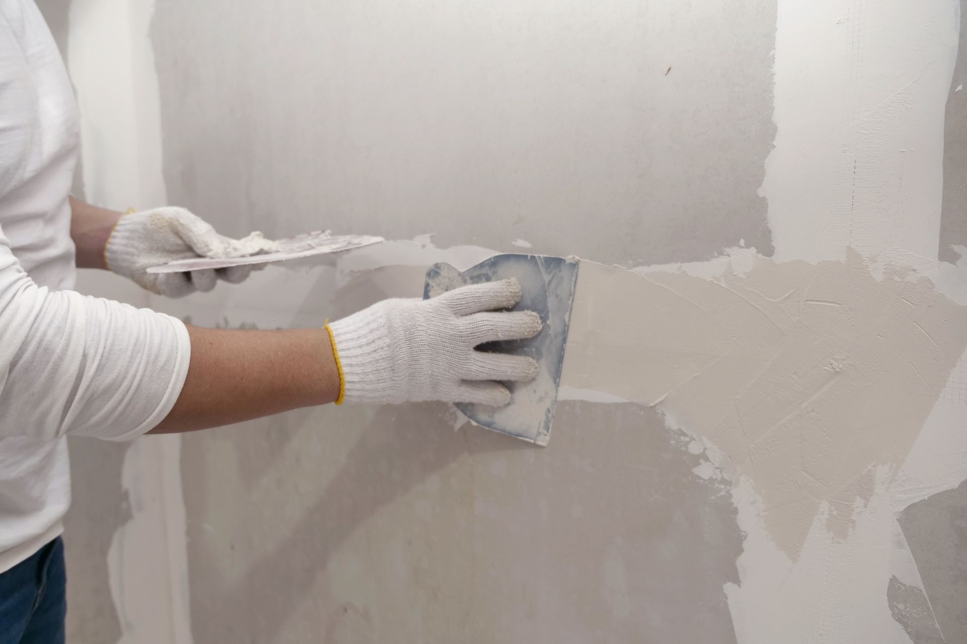 Person in white gloves using a trowel to apply drywall compound to a wall.