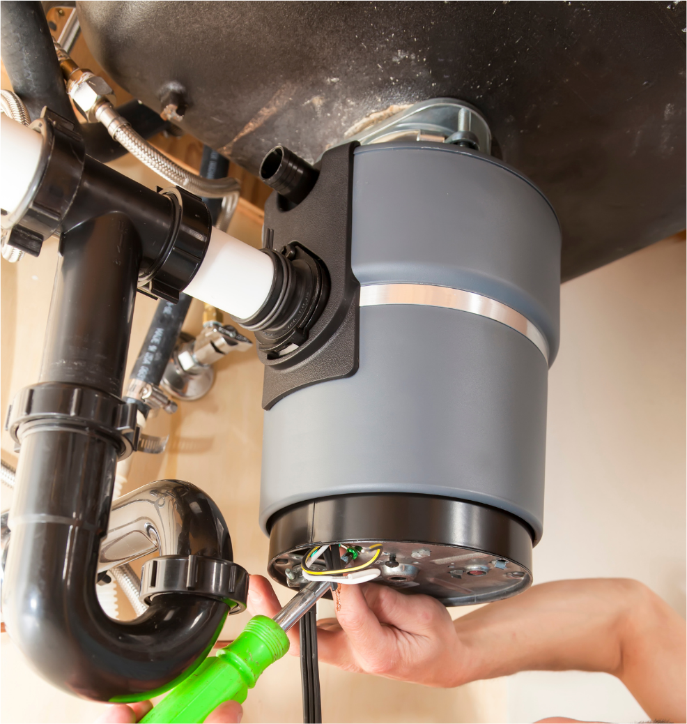 Hands using a screwdriver to install a gray garbage disposal under a sink.