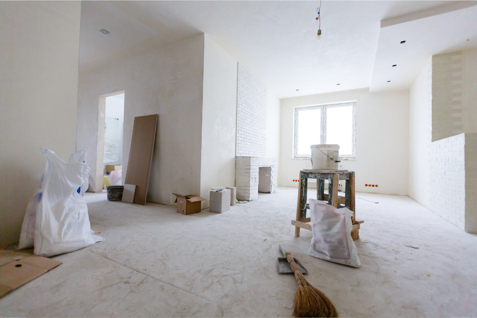 A partially renovated room with bare plaster walls, scattered construction materials, and an unfinished ceiling.