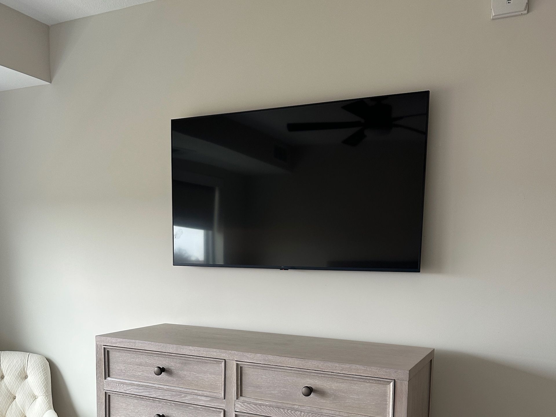 A large black TV mounted above a light-colored dresser on a light-colored wall.