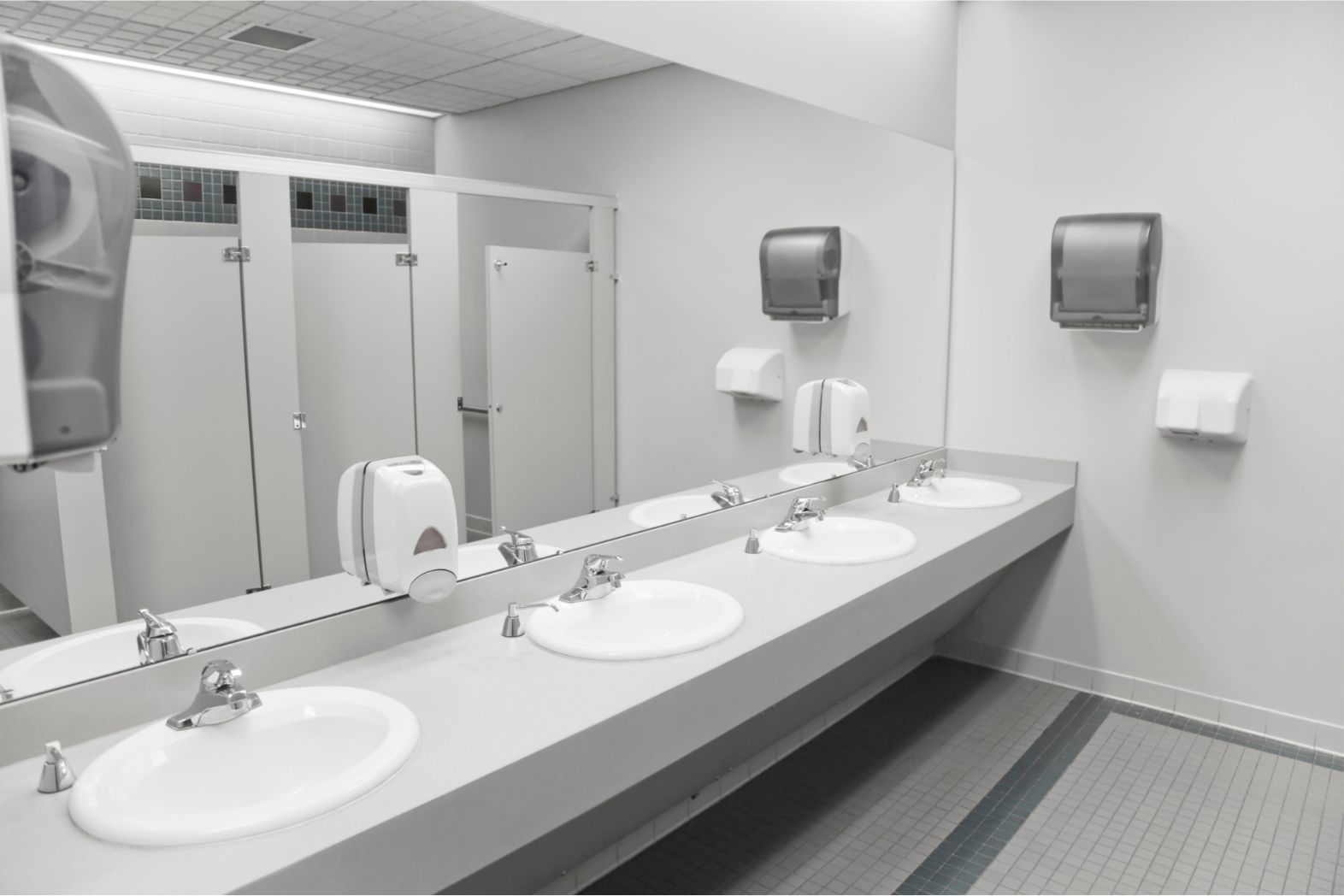 Modern public restroom with white sinks, mirrors, and hand dryers on gray walls