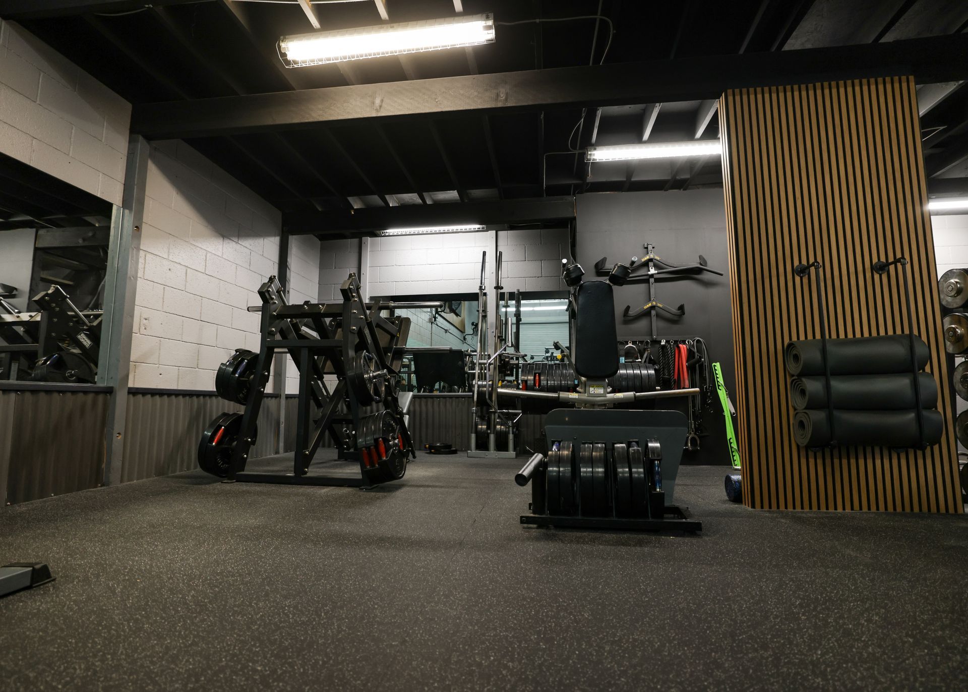 Gym interior with exercise equipment on a rubber floor; wooden accent wall.