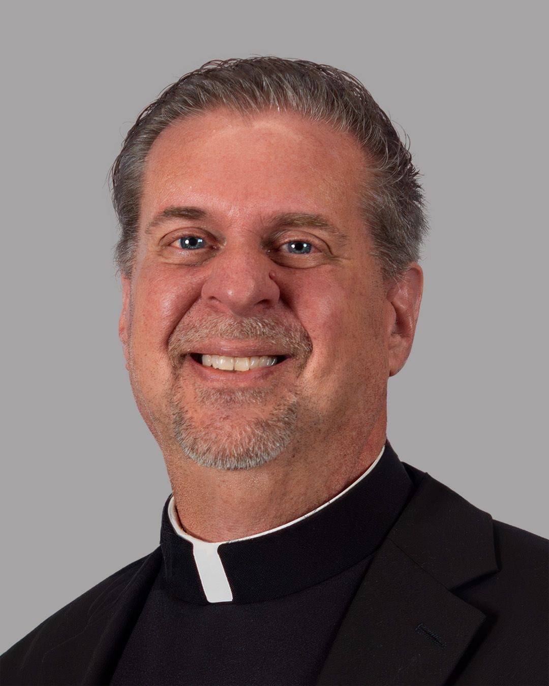 A man with a beard wearing a black suit and a clergy collar