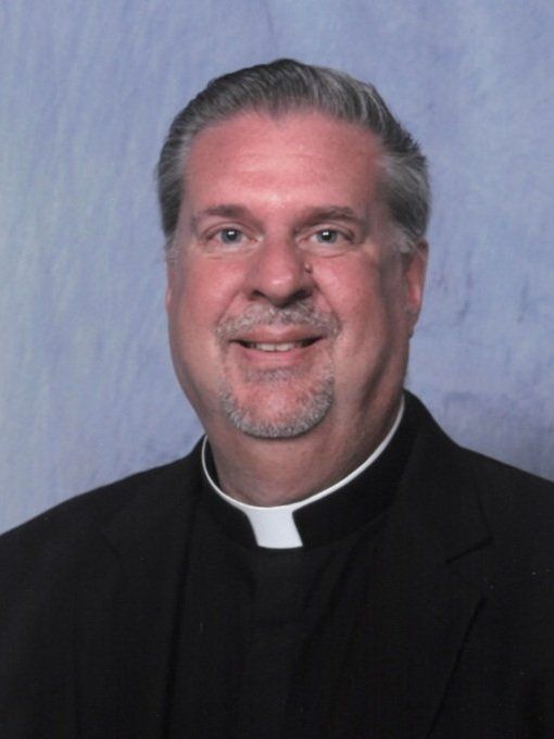 A man with a beard wearing a black suit and a clergy collar