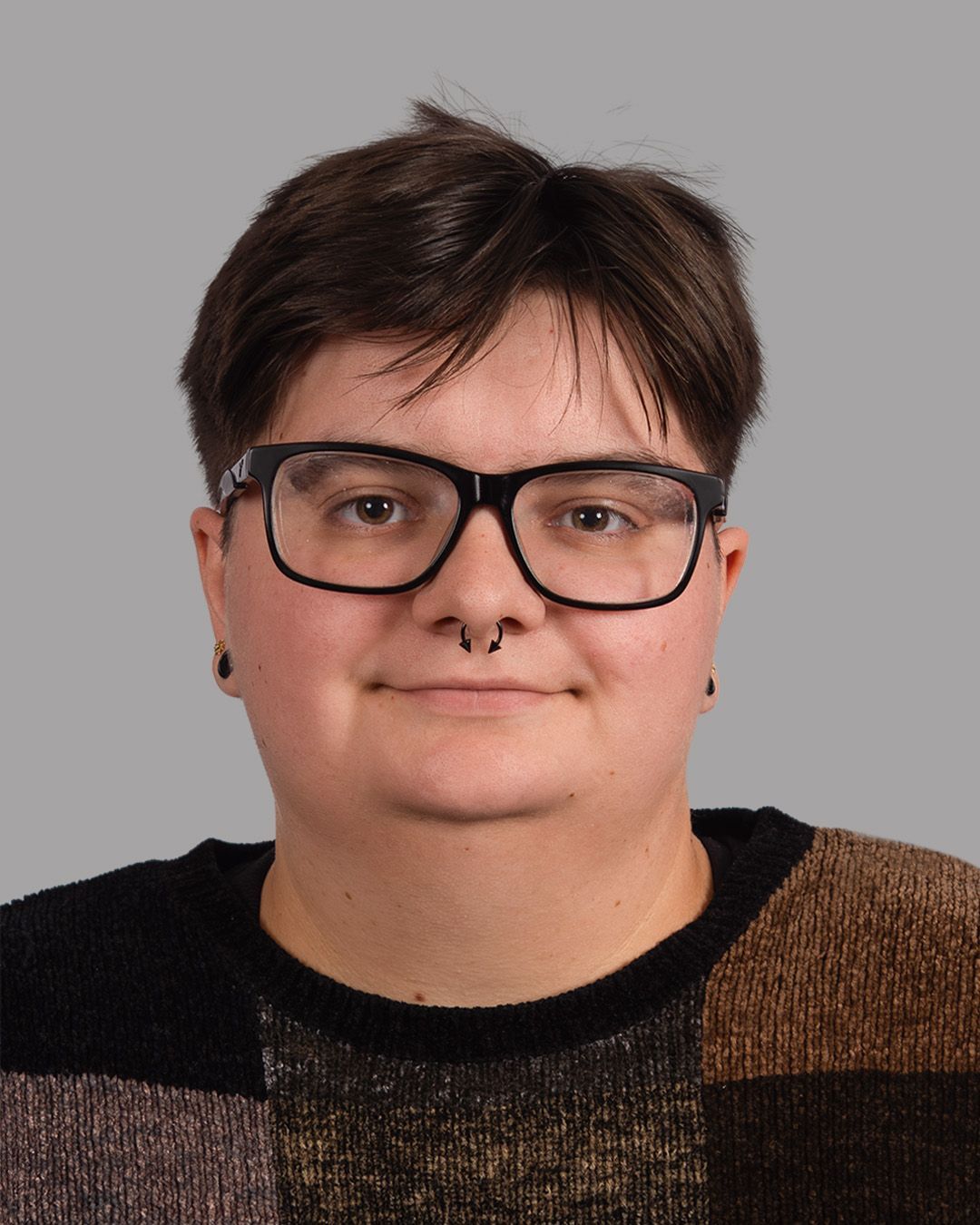 A woman wearing glasses and a nose ring is standing in front of a brick wall.